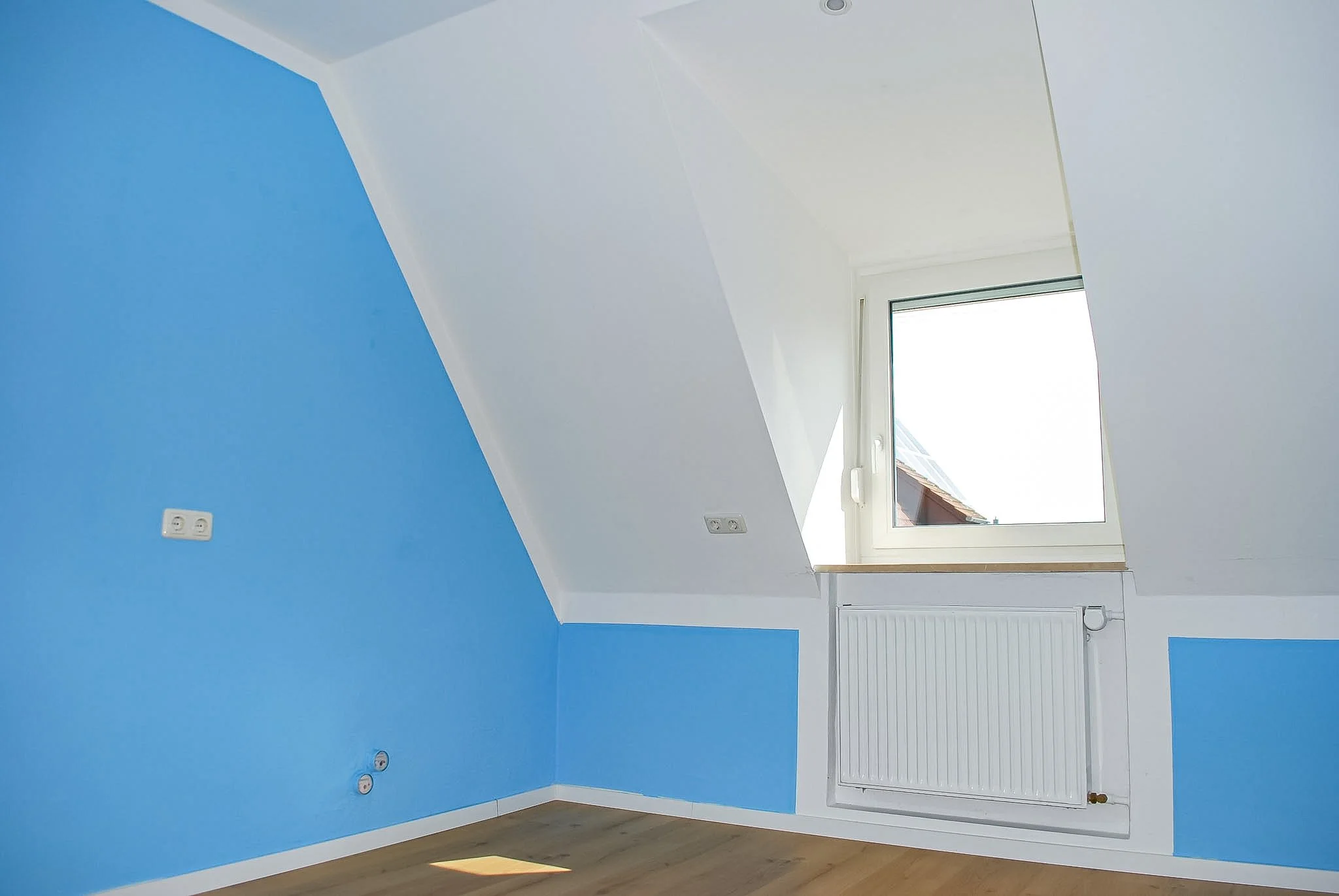 Ein weißes Zimmer mit blauer Wand, Fenster und Heizkörper.