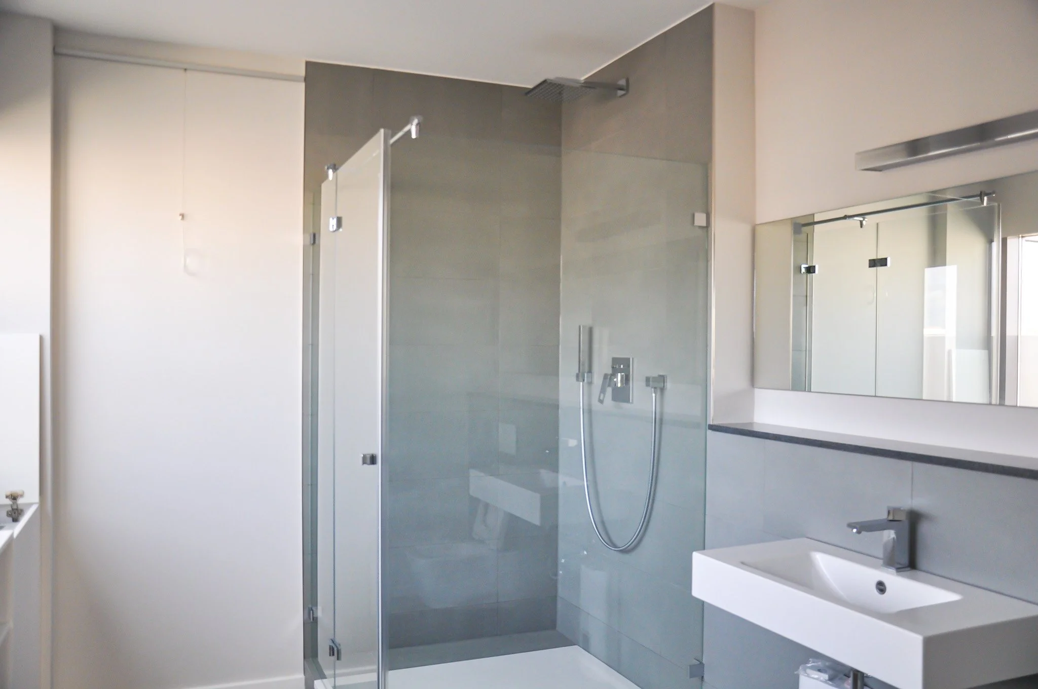 Modernes Badezimmer mit einer Glas-Duschtür, einer Wandspiegel, Waschbecken und einem Handtuchhalter.