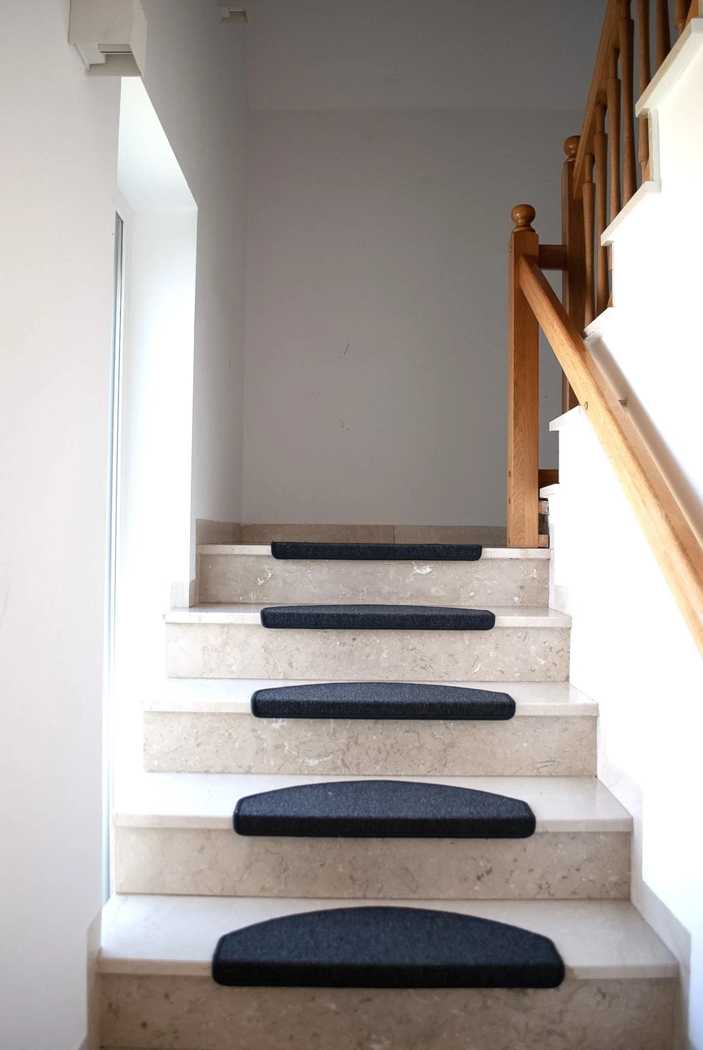 Innenansicht einer Treppe mit schwarzen rutschfesten Stufen und Holzhandlauf