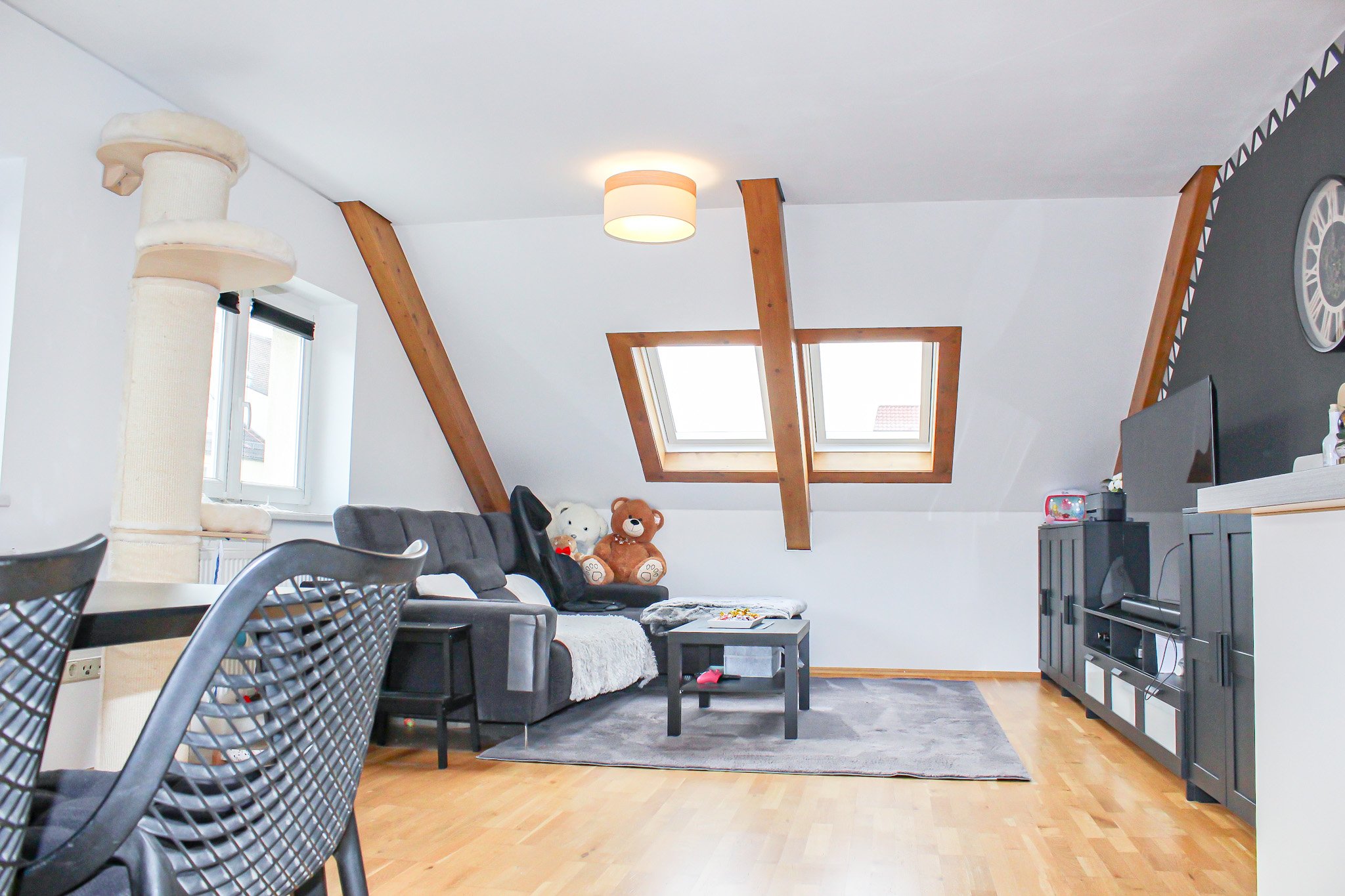 Blick in ein modernes Wohnzimmer mit Couch, Sessel, Kaffeetisch, Gardinen, Spielzeug und Fernseher. Dachfenster lassen natürliches Licht herein.