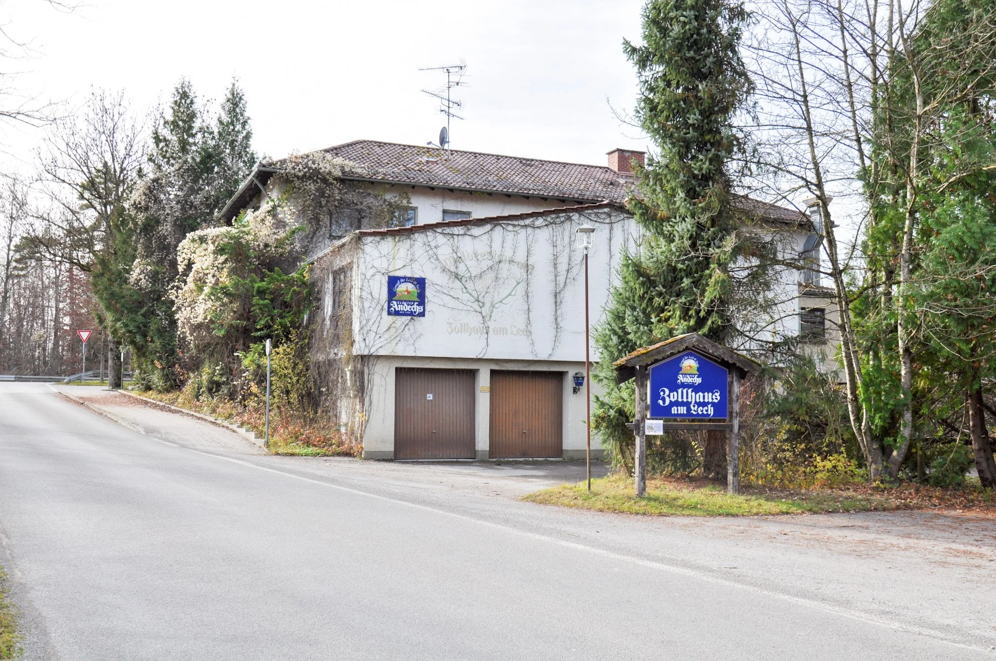 Ein Haus mit einem Schild und einem Tor, umgeben von Bäumen, in einer ländlichen Gegend.