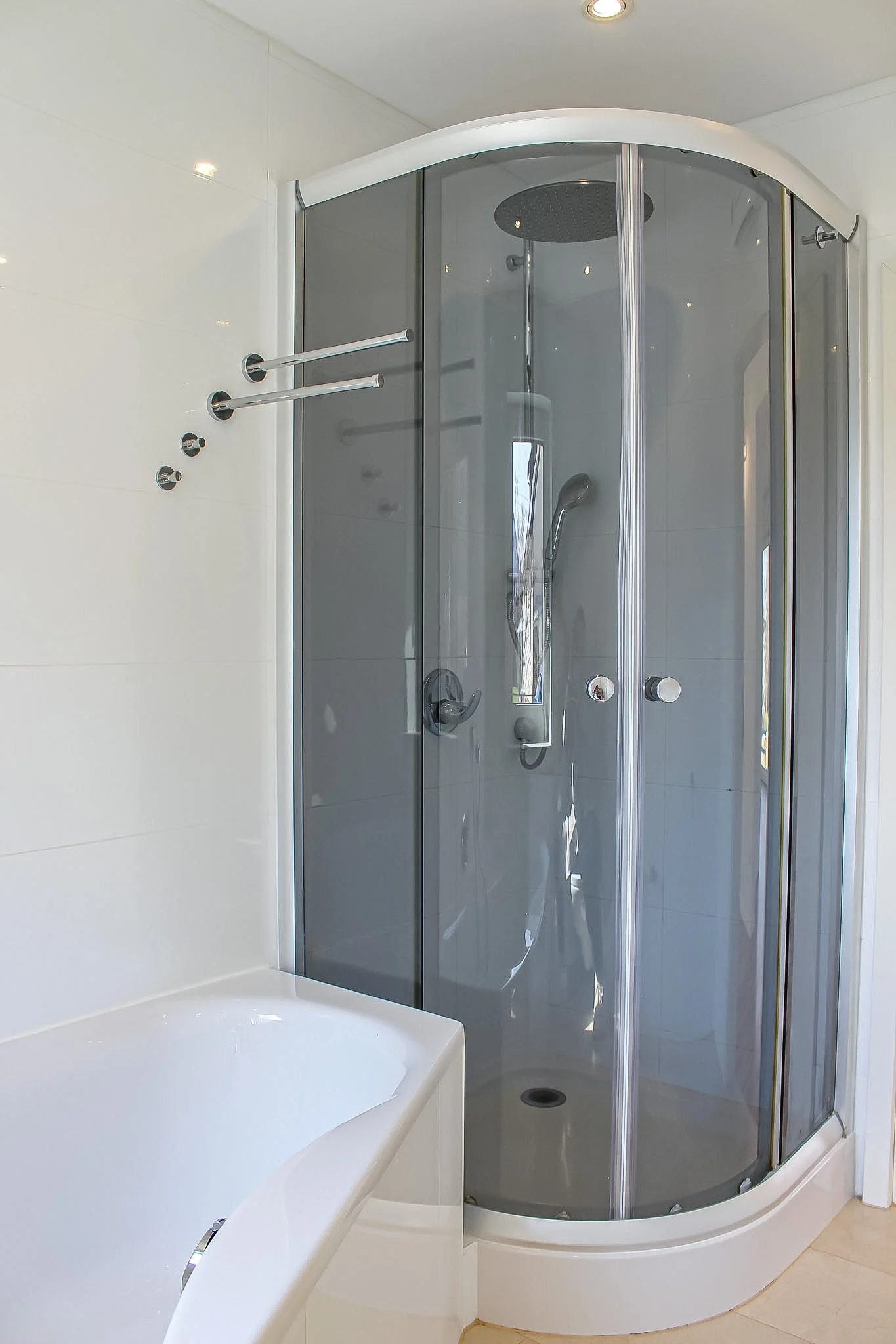 Modernes Badezimmer mit einer begehbaren Dusche mit Glaswänden und einem Regenschauerkopf, daneben eine Badewanne.