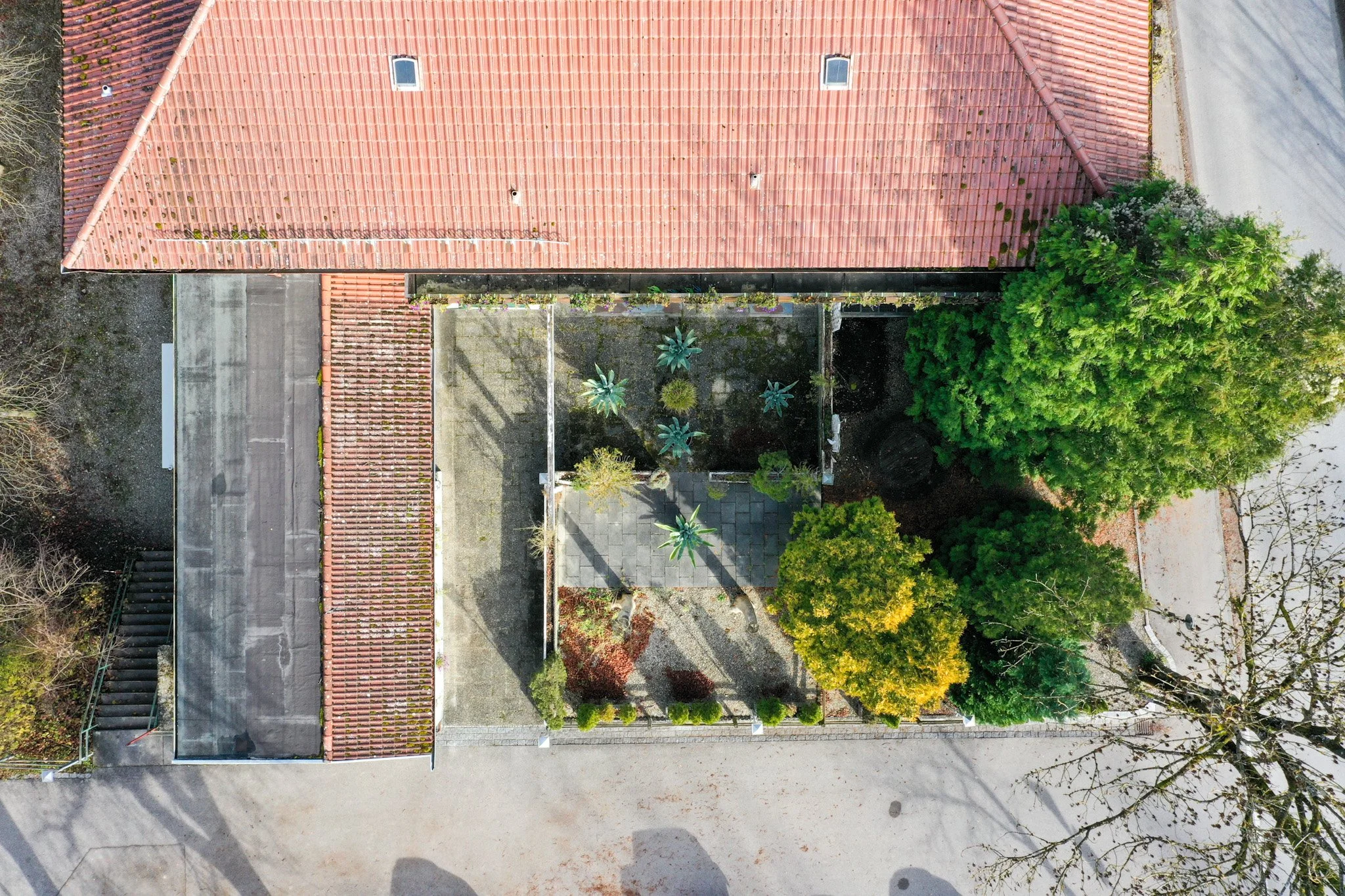 Luftaufnahme eines Daches mit roten Ziegeln, umgeben von Bäumen und einer urbanen Umgebung.