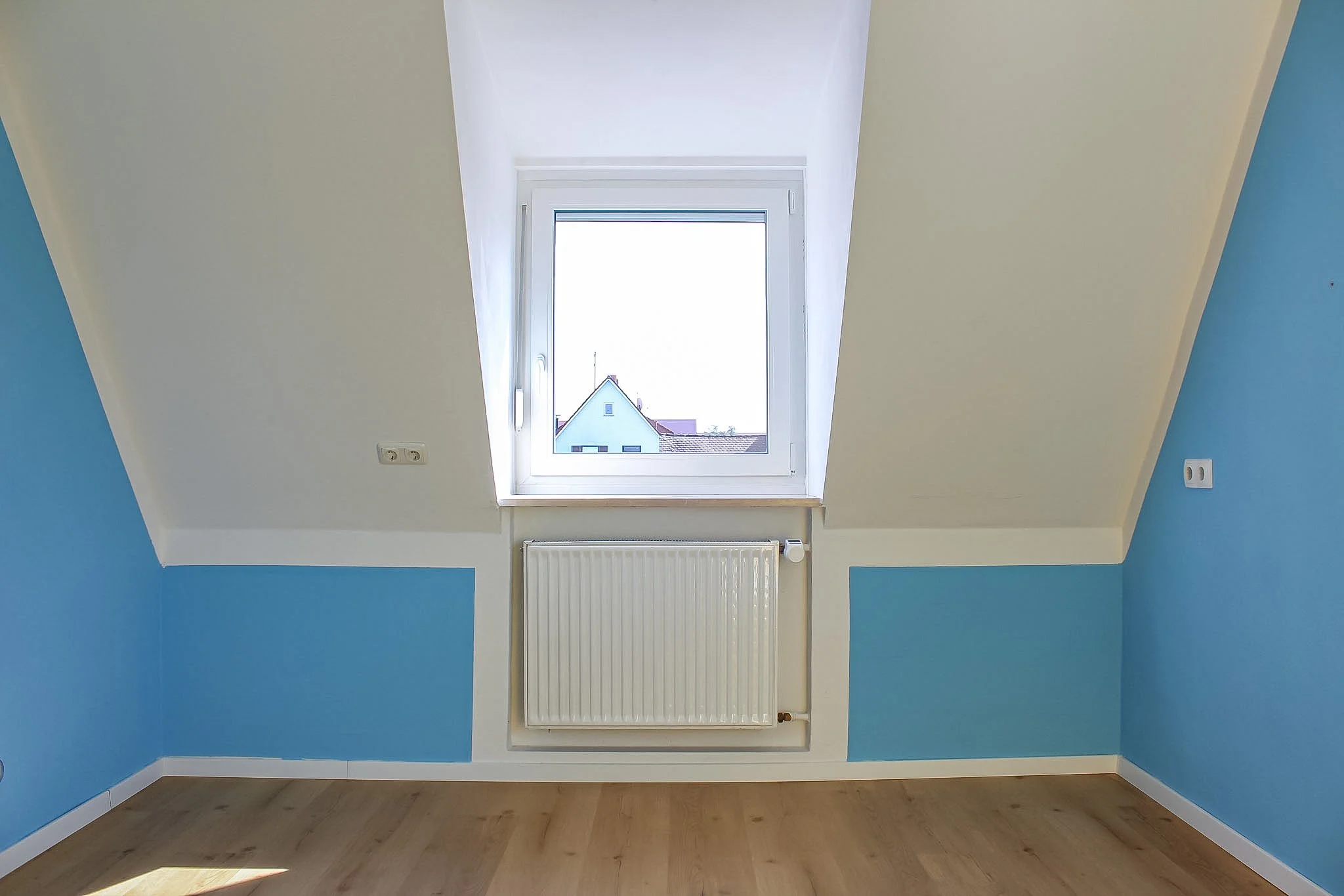 Ein leerer Raum mit blauen Wänden, einer weißen Decke, einem weißen Fenster, Heizkörper und Holzfußboden.