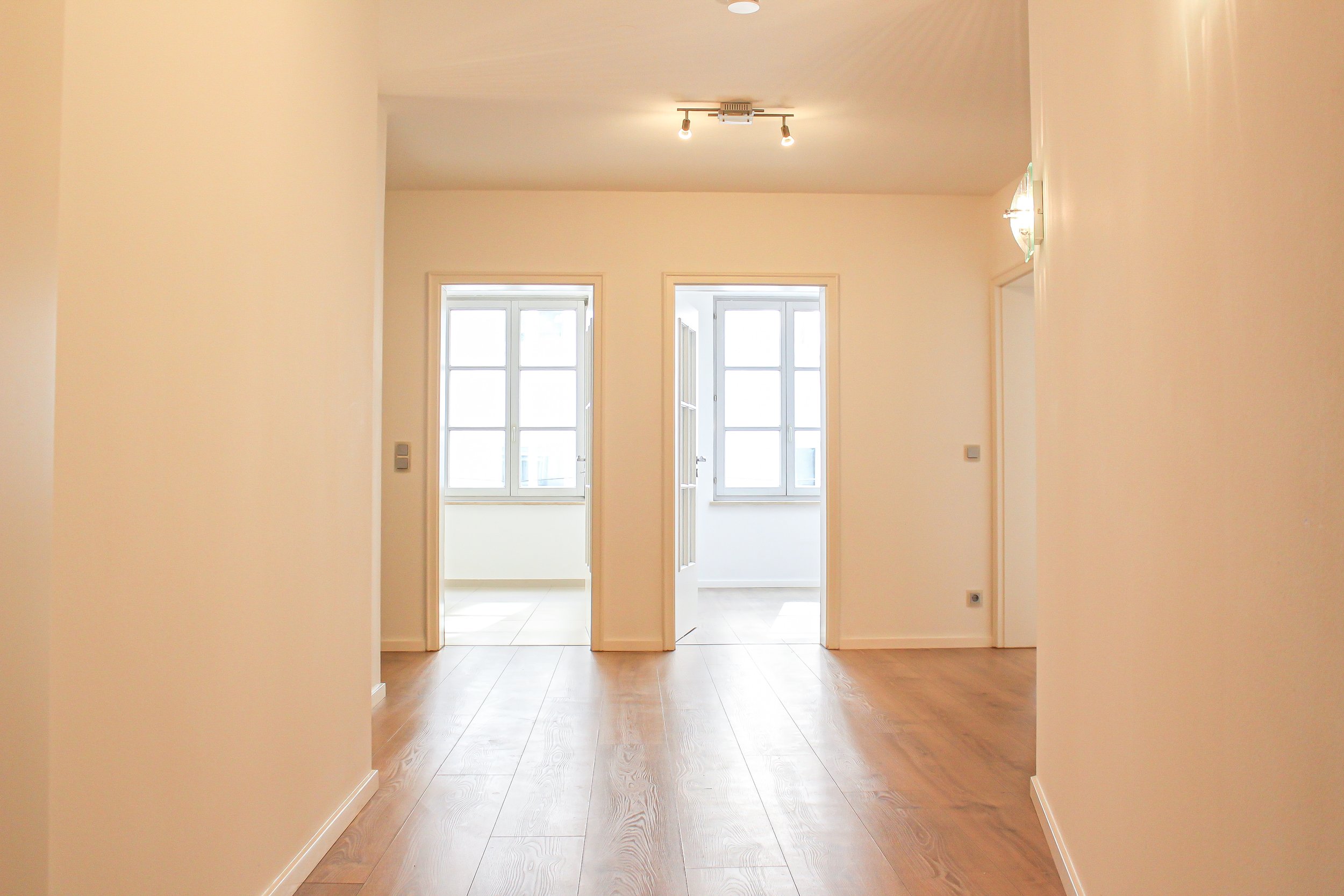 Heller Flur mit zwei offenen Türen zu Räumen mit Fenstern, Holzboden und weiß gestrichenem Raum.