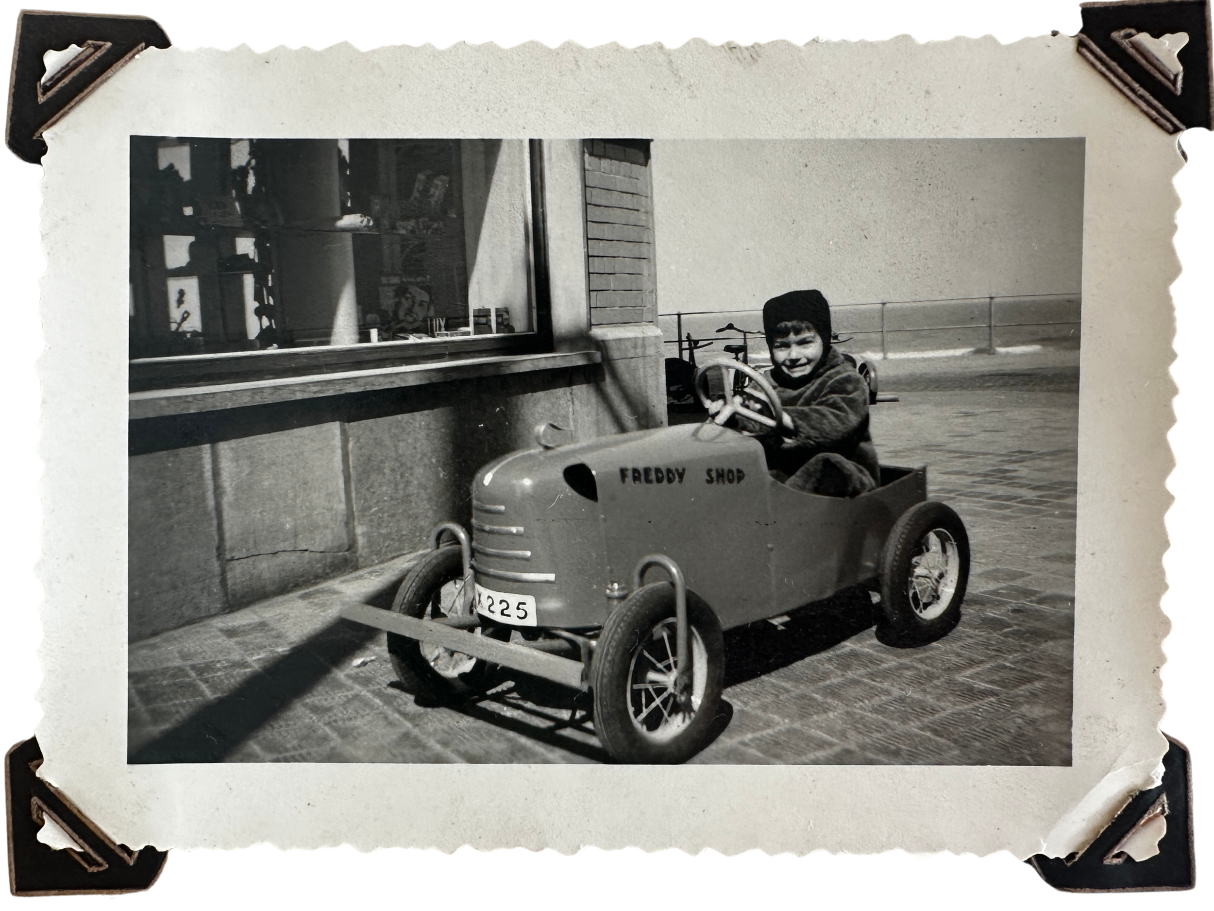 Een jonge jongen rijdt in een speelgoedautootje met de tekst 'FREDDY SHOP' op de zijkant