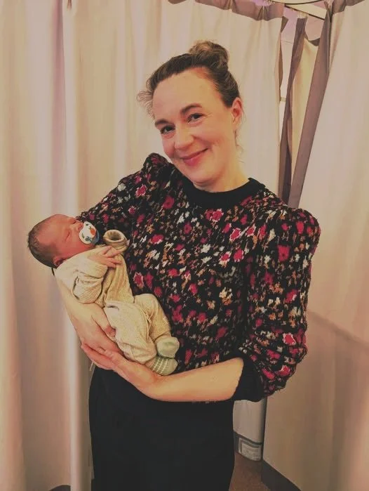 Smiling mother holding a newborn baby, showing early bonding and gentle support.