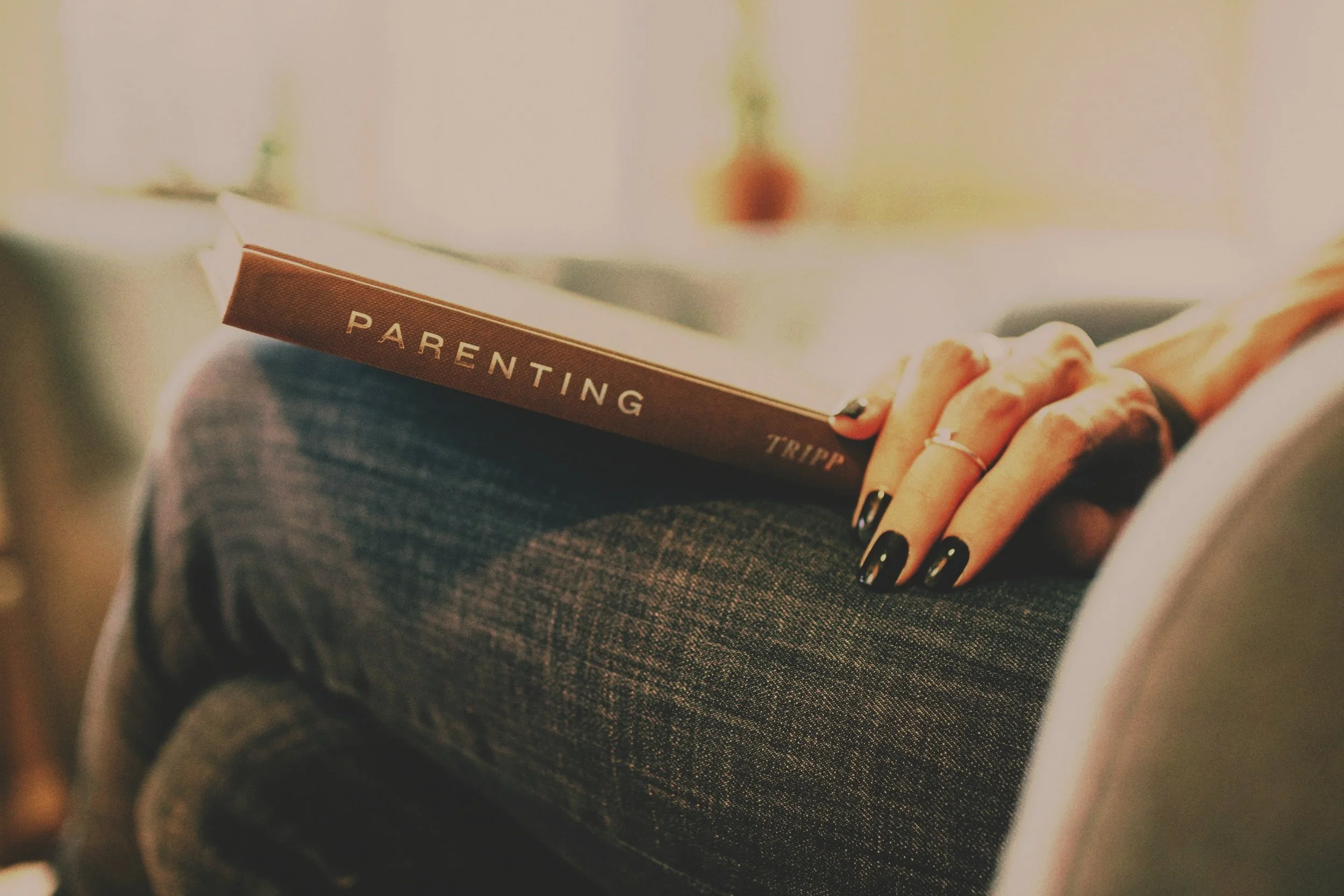 Close-up of someone holding a parenting book while seated, representing guidance and learning.