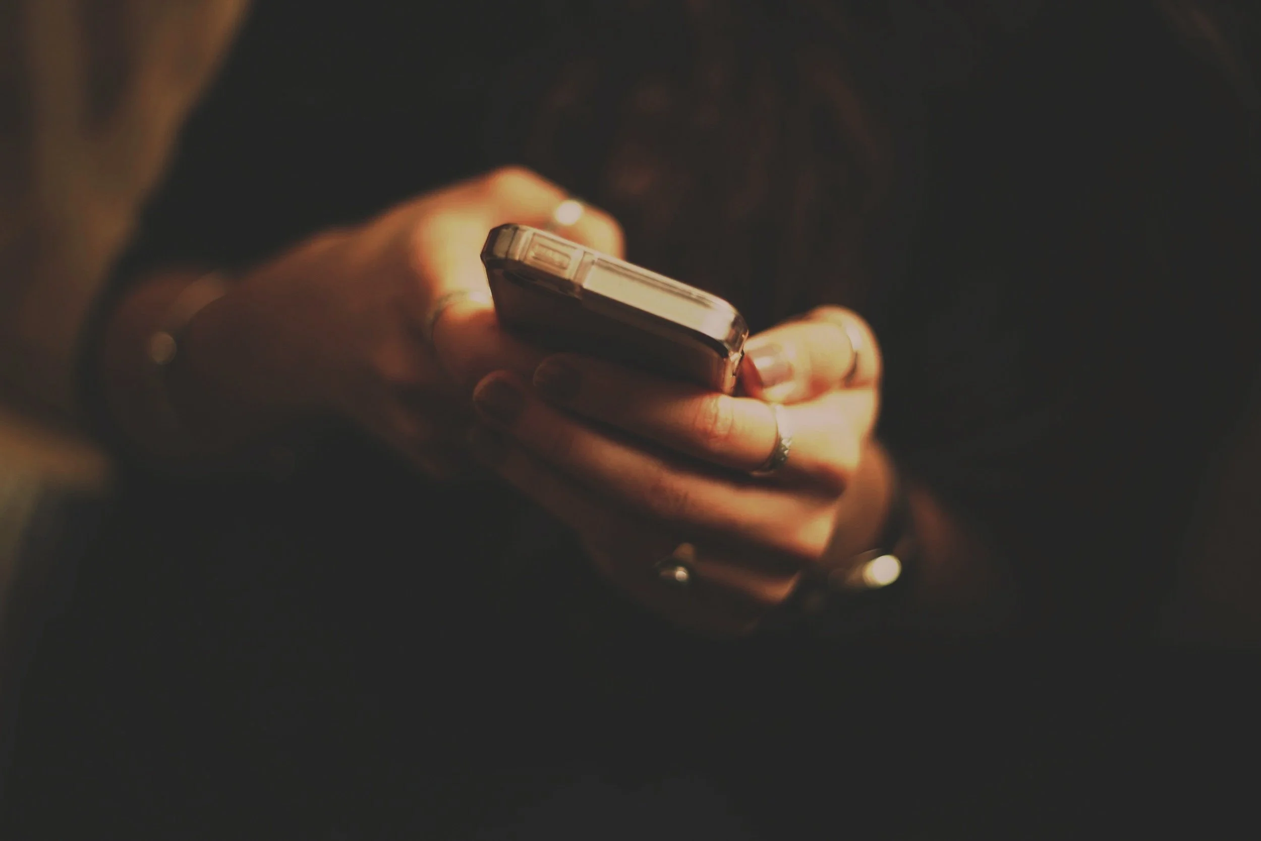 Close-up of a person's hand holding a smartphone in a dimly lit environment.