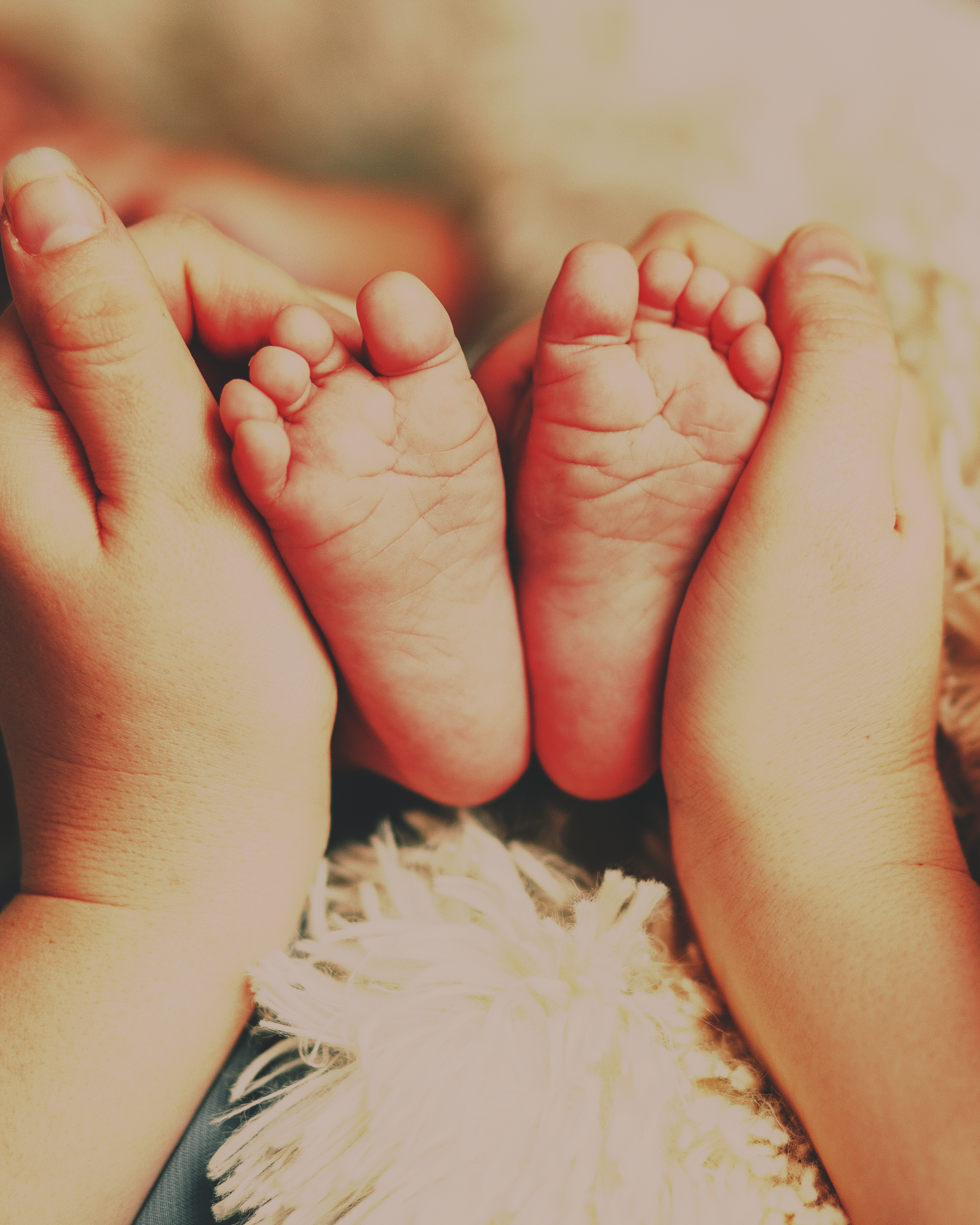 Adult hands holding two tiny baby feet with a furry white blanket below.