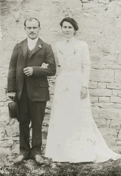 Un homme et une femme en vêtements anciens, posant ensemble devant un mur en pierre.