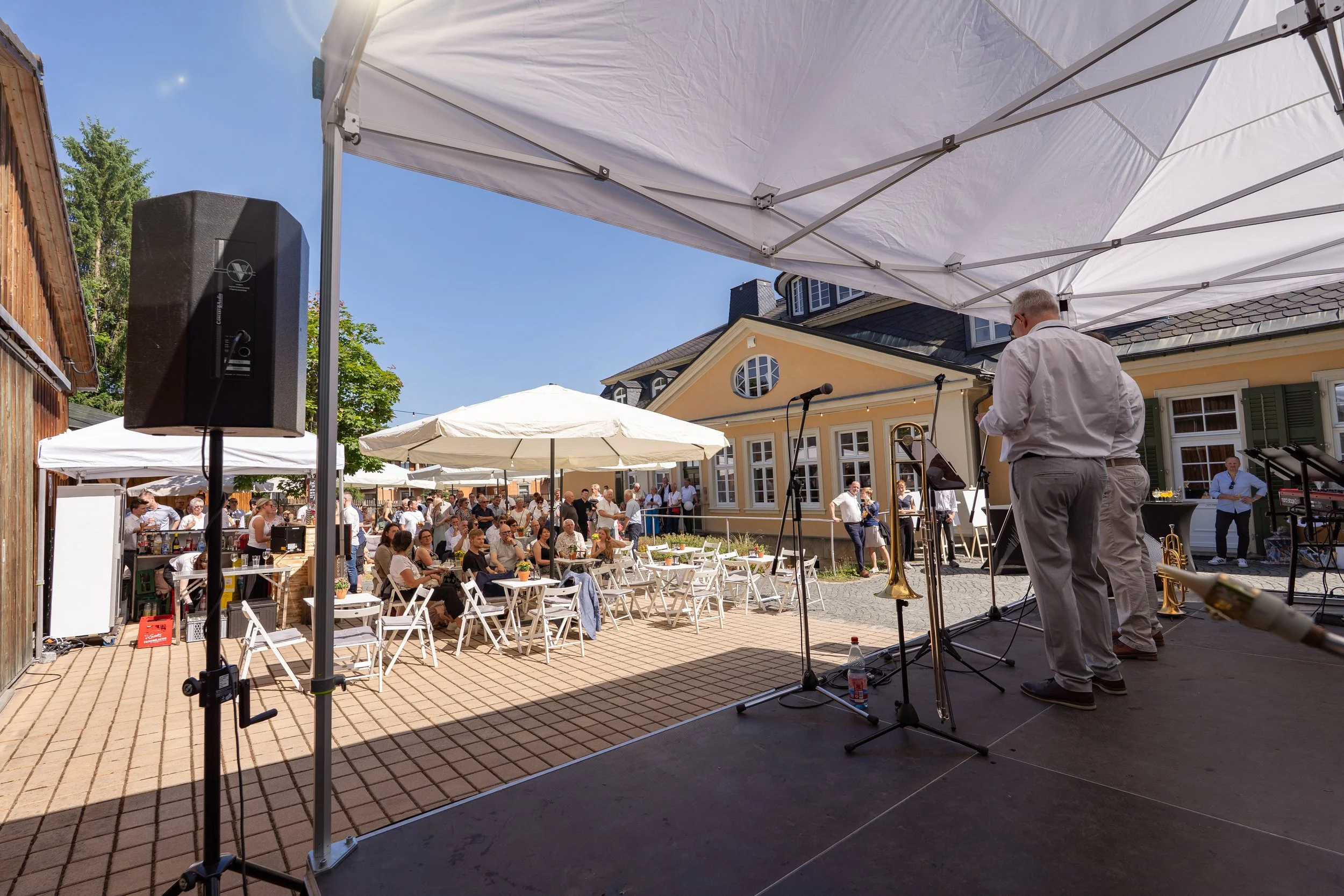 Unternehmensevent - Geschäftsführer sprechen auf Bühne vor Gsten ihres Sommerfests, blauer Himmel und Firmengebäude im Hintergrund - Markenfotografie Culet