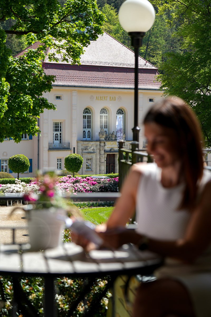Markenkampagne Staatsbad Bad Elster - Frau liest lächelnd ein Buch im Vordergrund, historisches Staatsbad im Hintergrund - Culet