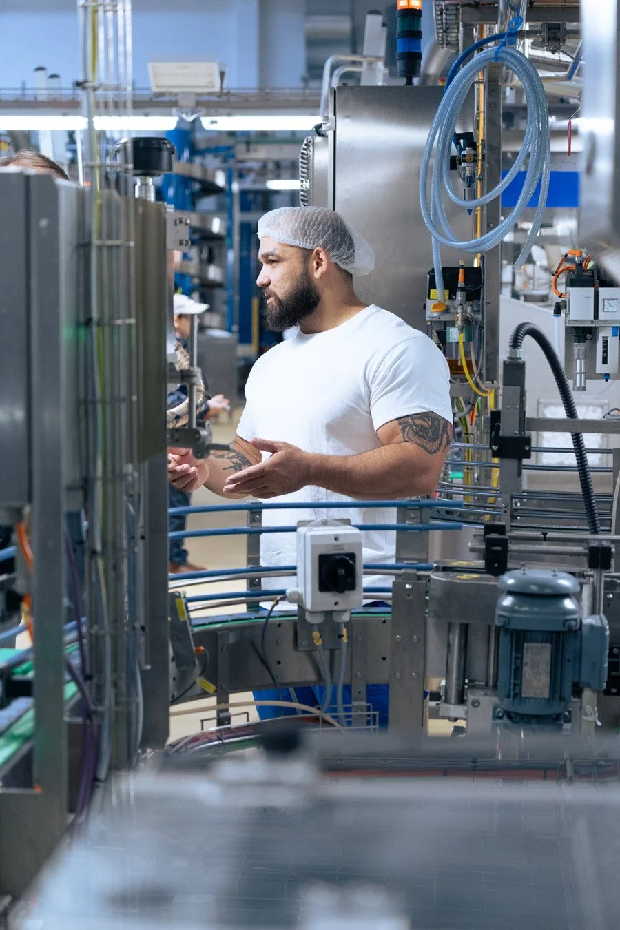 Industriereportage Tetra Pak - Mitarbeiter mit Haarnetz erklärt Produktionsablauf in der Halle - Culet