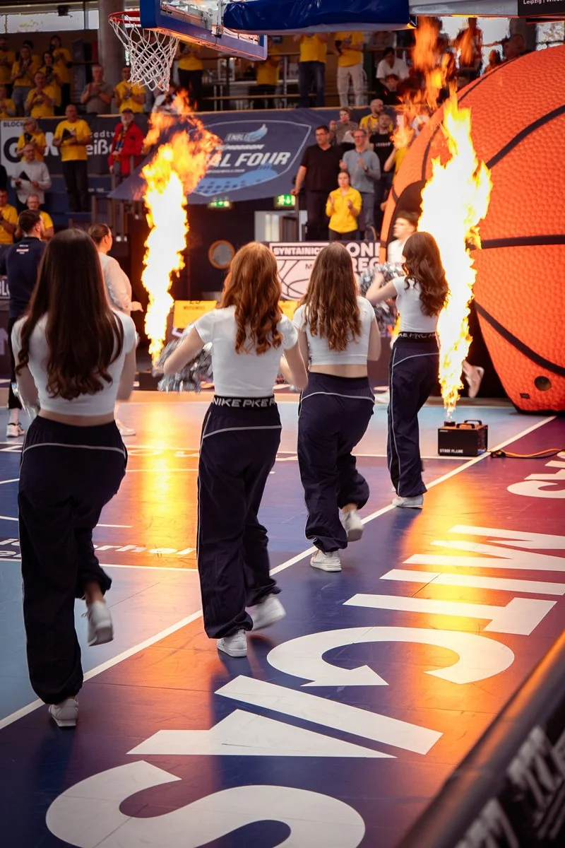 Livefotografie ENBL Basketball - Cheerleader vor Feuerfontänen beim Einlauf der Mannschaft, Logo vom Sponsor im Vordergrund - Livefotografie Culet