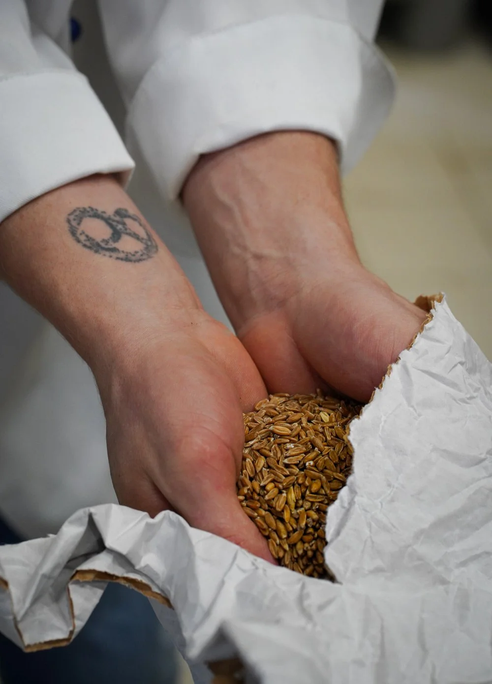 Markenkampagne Wunderlichs Backstuben - Detailaufnahme Hände mit Getreidekörnern, Brezel-Tattoo auf dem Handgelenk - Handwerksfotografie - Culet