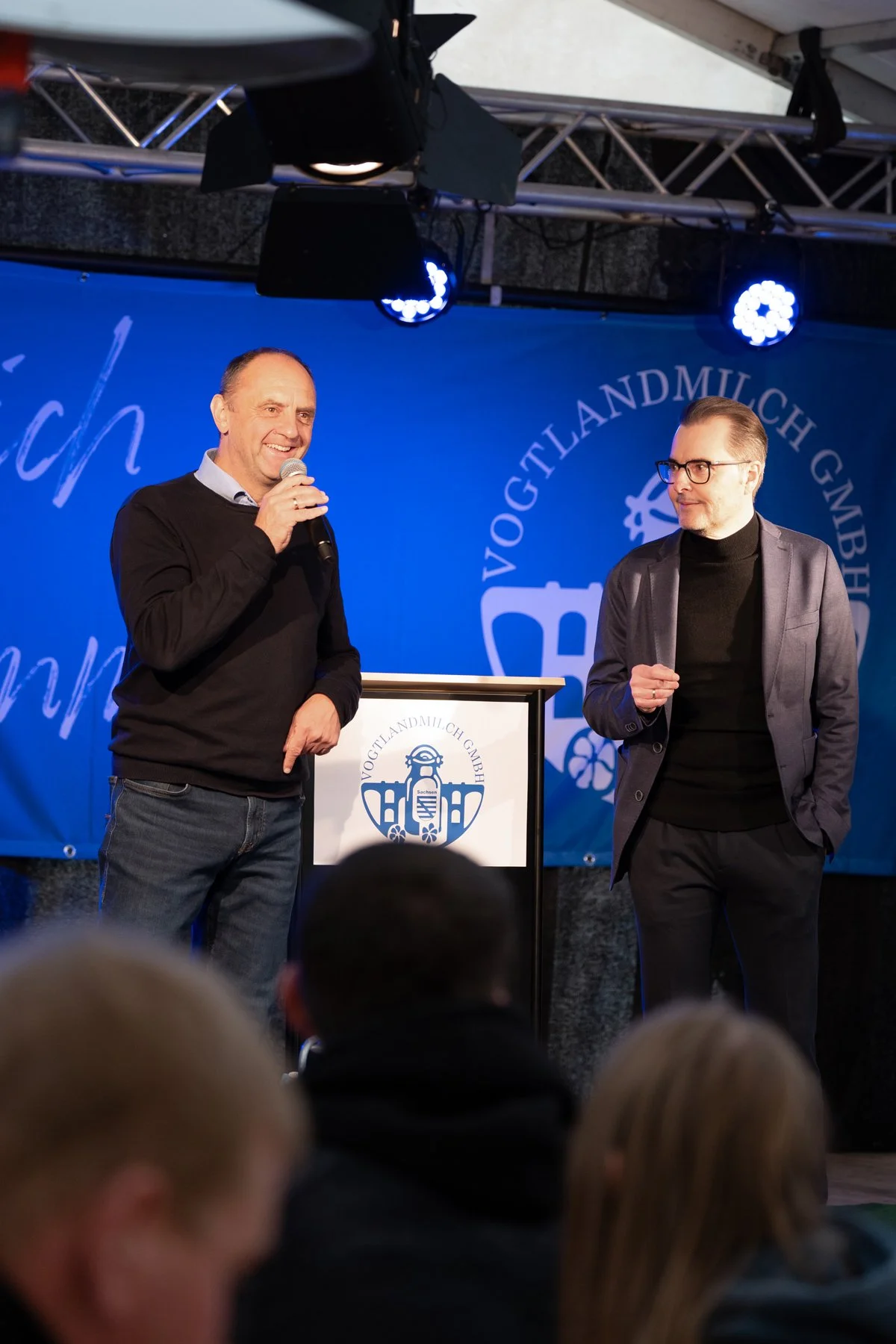 Zwei Geschäftsführer stehen an einem Podium auf einer Bühne und halten eine Rede vor Publikum bei einer Unternehmensveranstaltung - authentische Businessfotografie von Culet