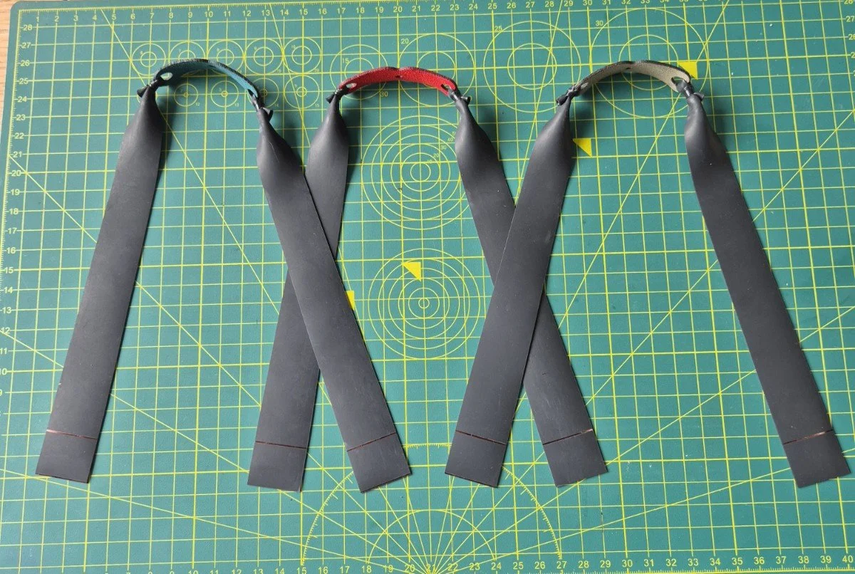 Three custom-made slingshot band sets resting on a green workshop cutting mat.