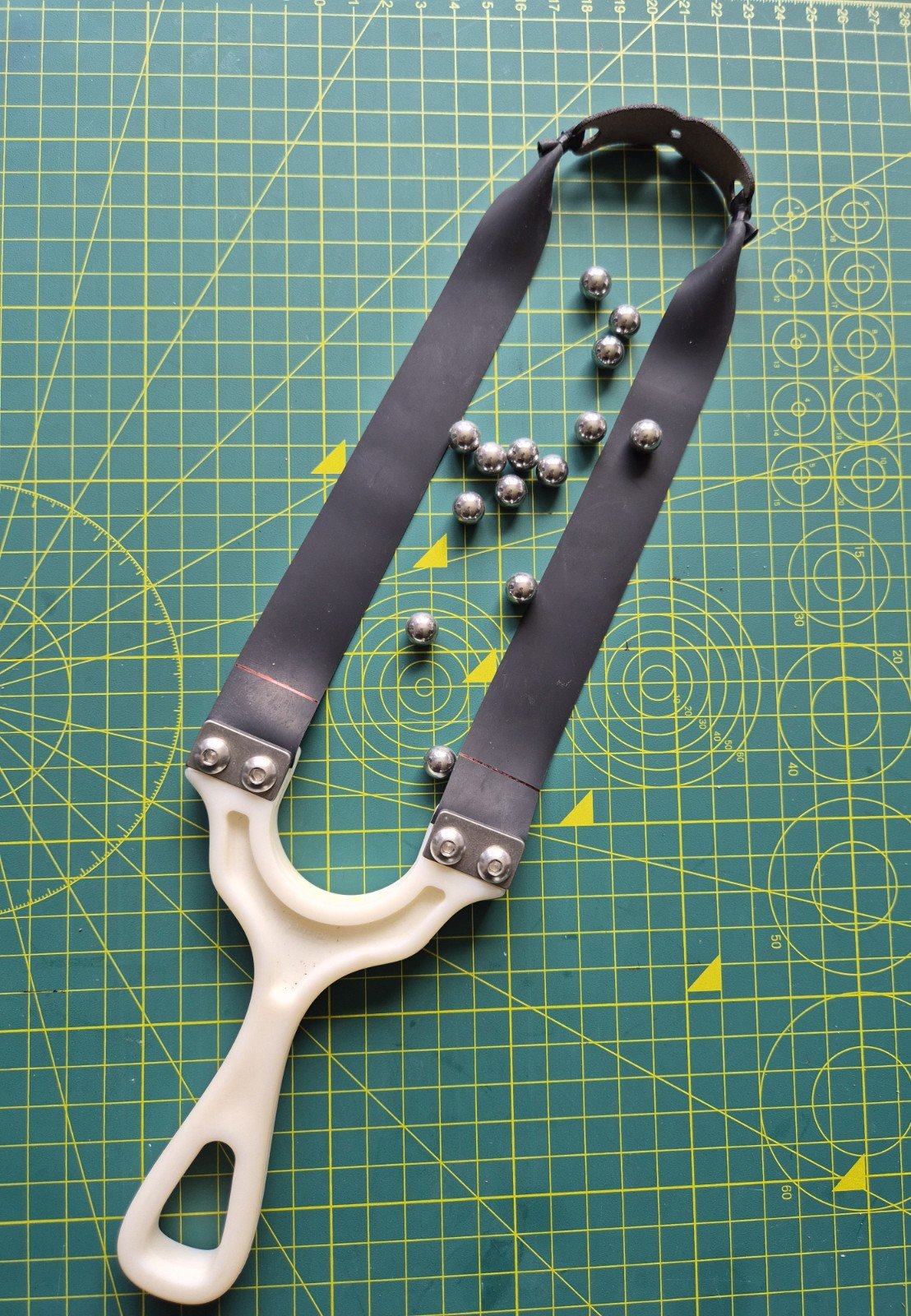 White slingshot frame rigged with black high-performance flat bands and steel ammo.