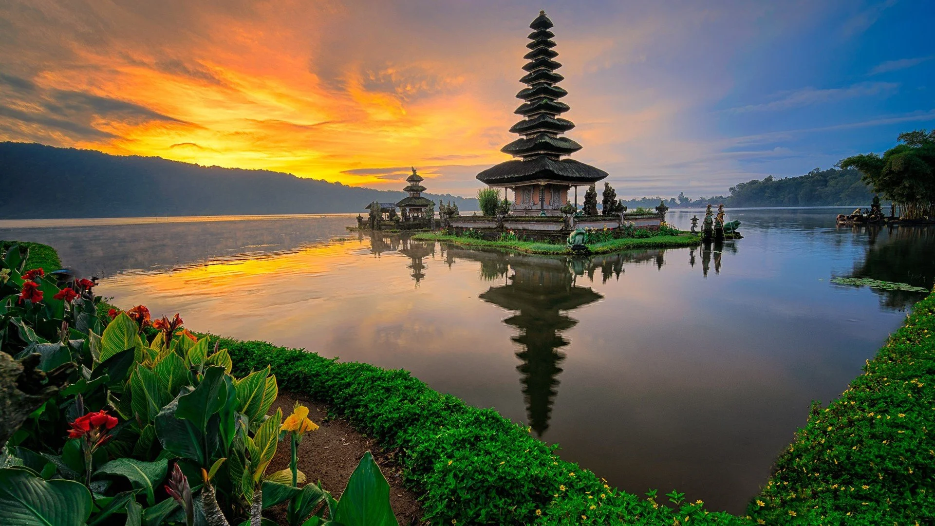 A serene lake sunset with traditional Balinese temples on small islands, surrounded by lush greenery and colorful flowers.