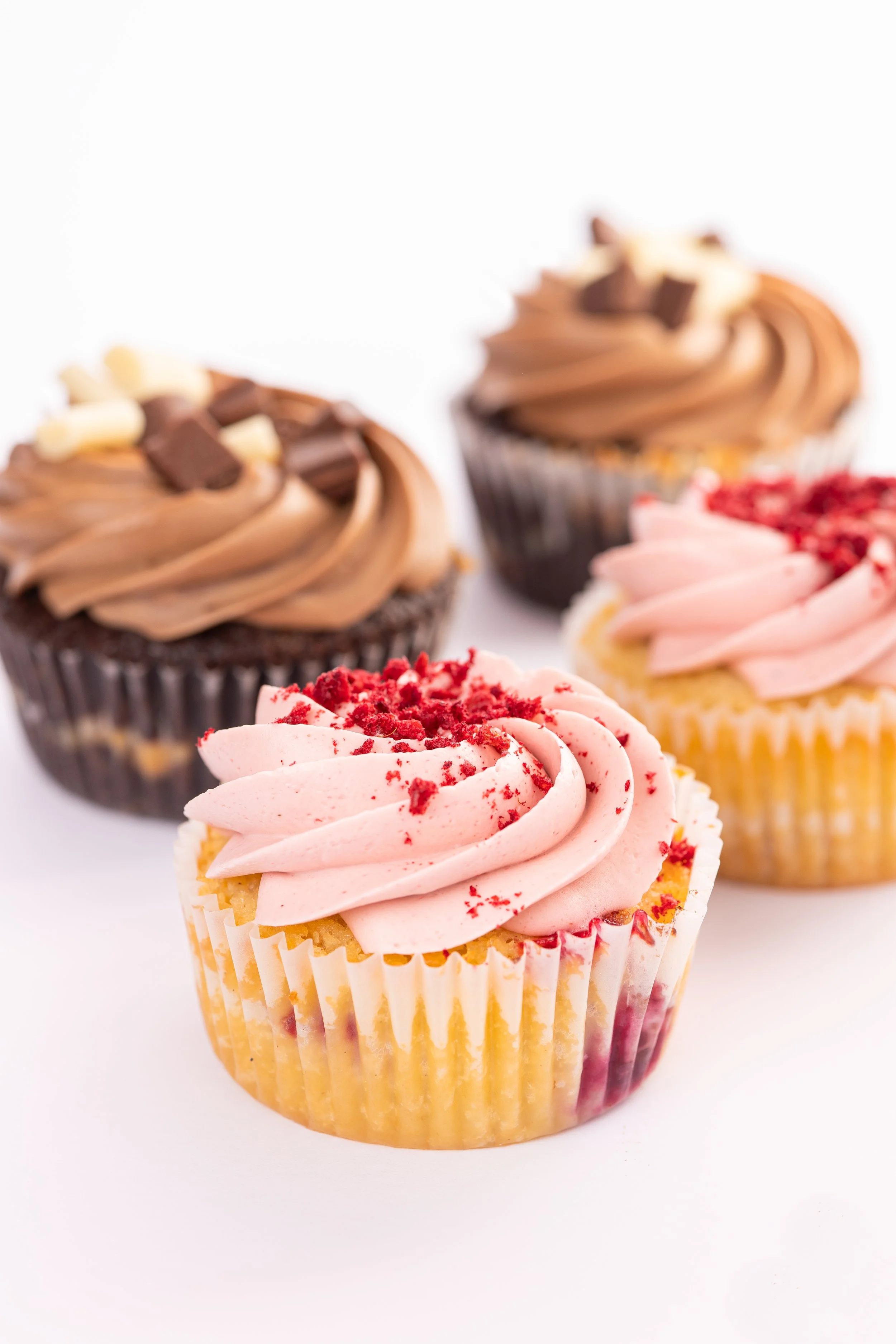 Cupcakes mit rosa und schokoladiger Buttercreme-Dekoration auf weißem Hintergrund.