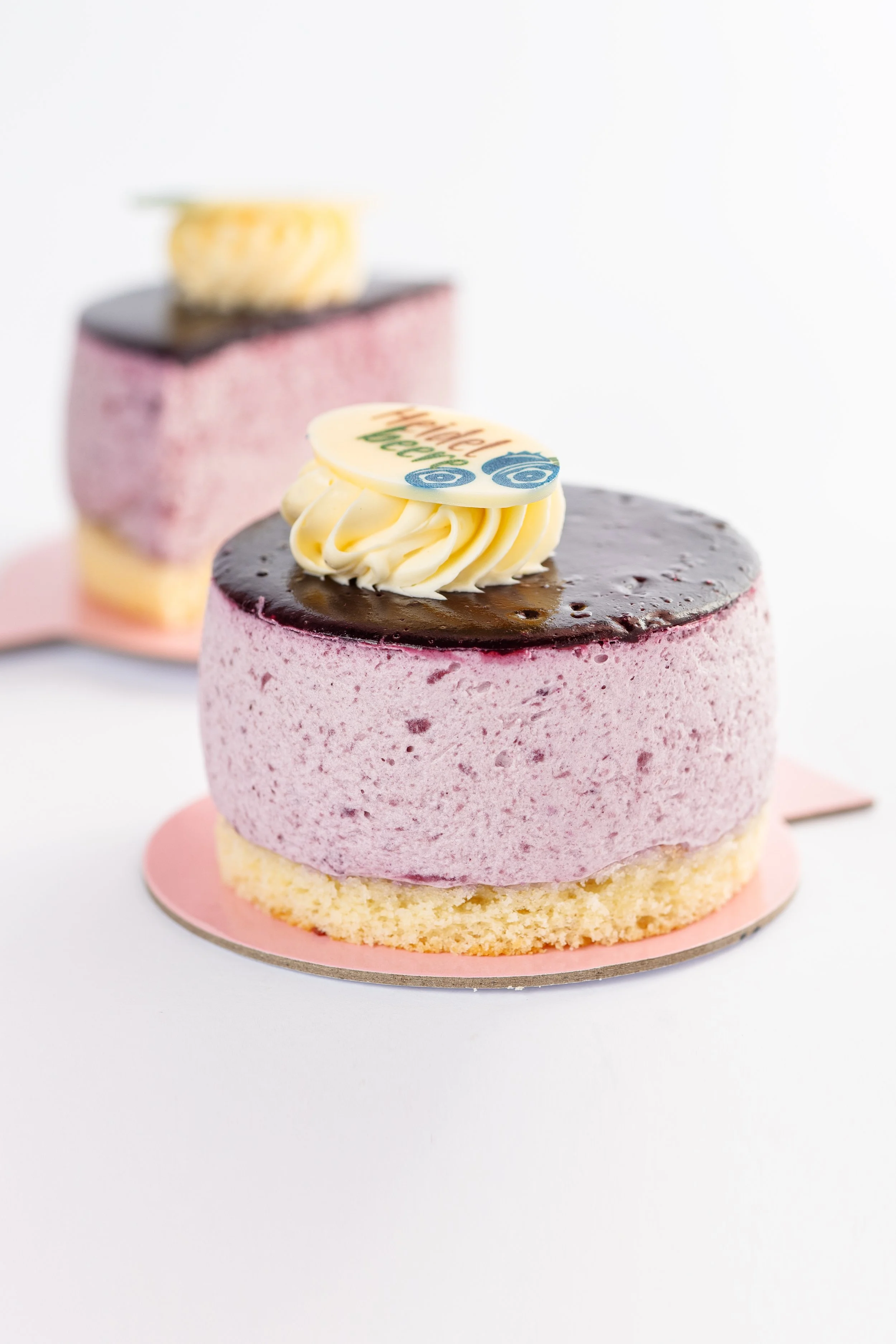 Kleiner Kuchen mit rosa Biskuitboden, lila Creme, Schokoladenglasur und Dekoration mit weißer Schokolade, die den Text 'Wunderschöner Bär' trägt.