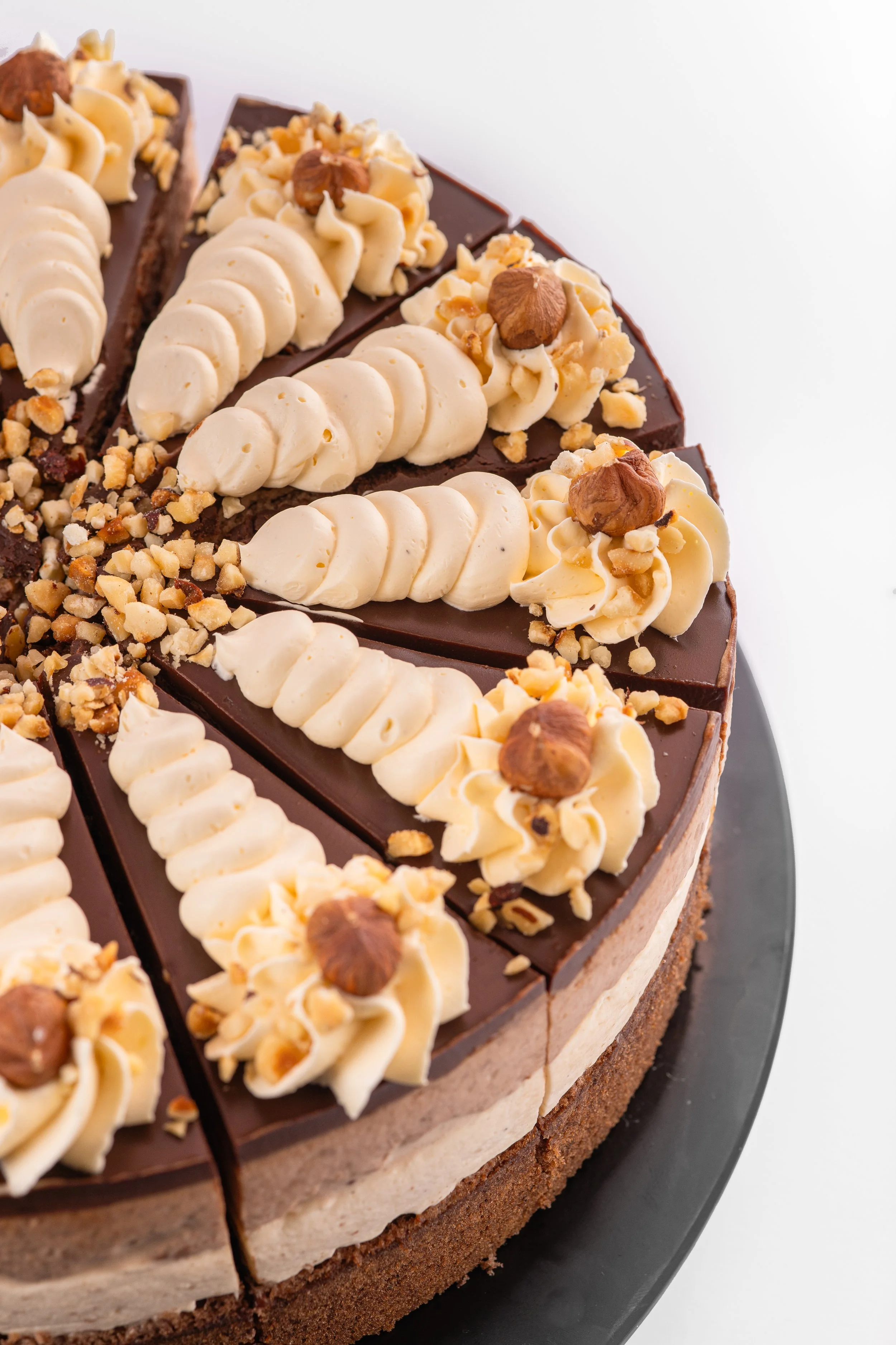 Schokoladenkuchen mit Ganache, Marshmallow, gehackten Nüssen und Schlagsahne auf einer dunklen Platte.