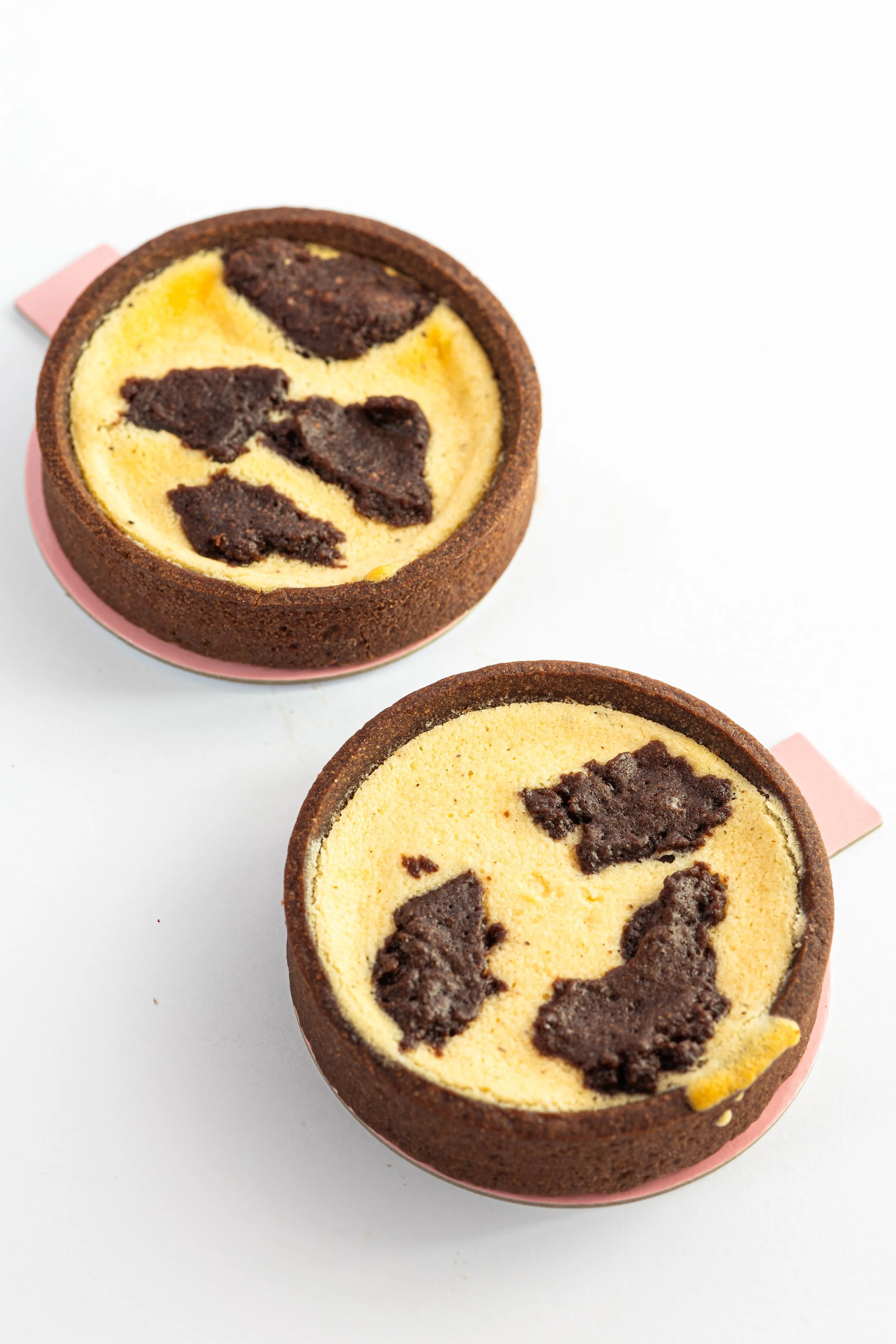 Zwei kleine Kuchen mit dunklen Schokoladenstücken auf weißem Hintergrund.