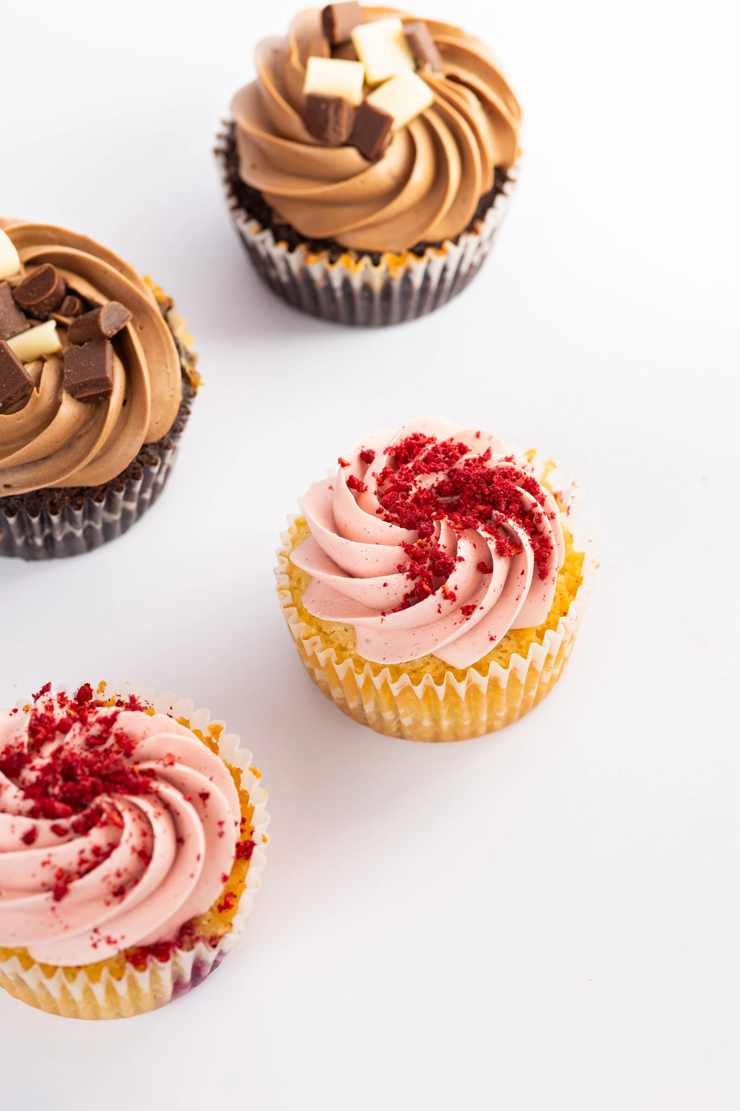 Vier Cupcakes mit Zuckerguss, zwei Schokoladen-Cupcakes und zwei Erdbeer-Cupcakes, auf weißem Hintergrund