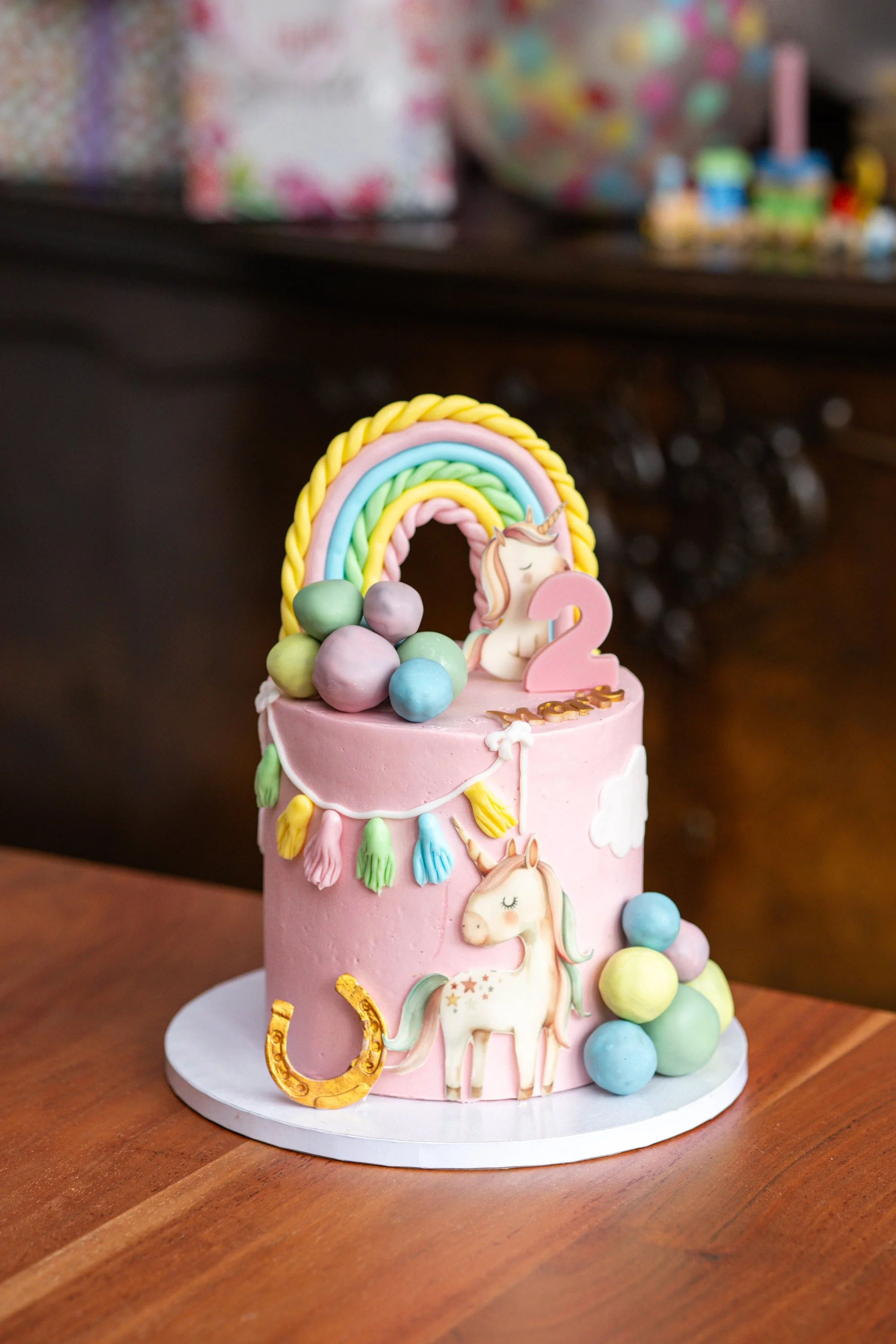 Ein pinker Geburtstagskuchen mit Einhorn Dekorationen, einem Regenbogen, bunten Ballons und einer Zahl 2, für einen zweijährigen Geburtstag.