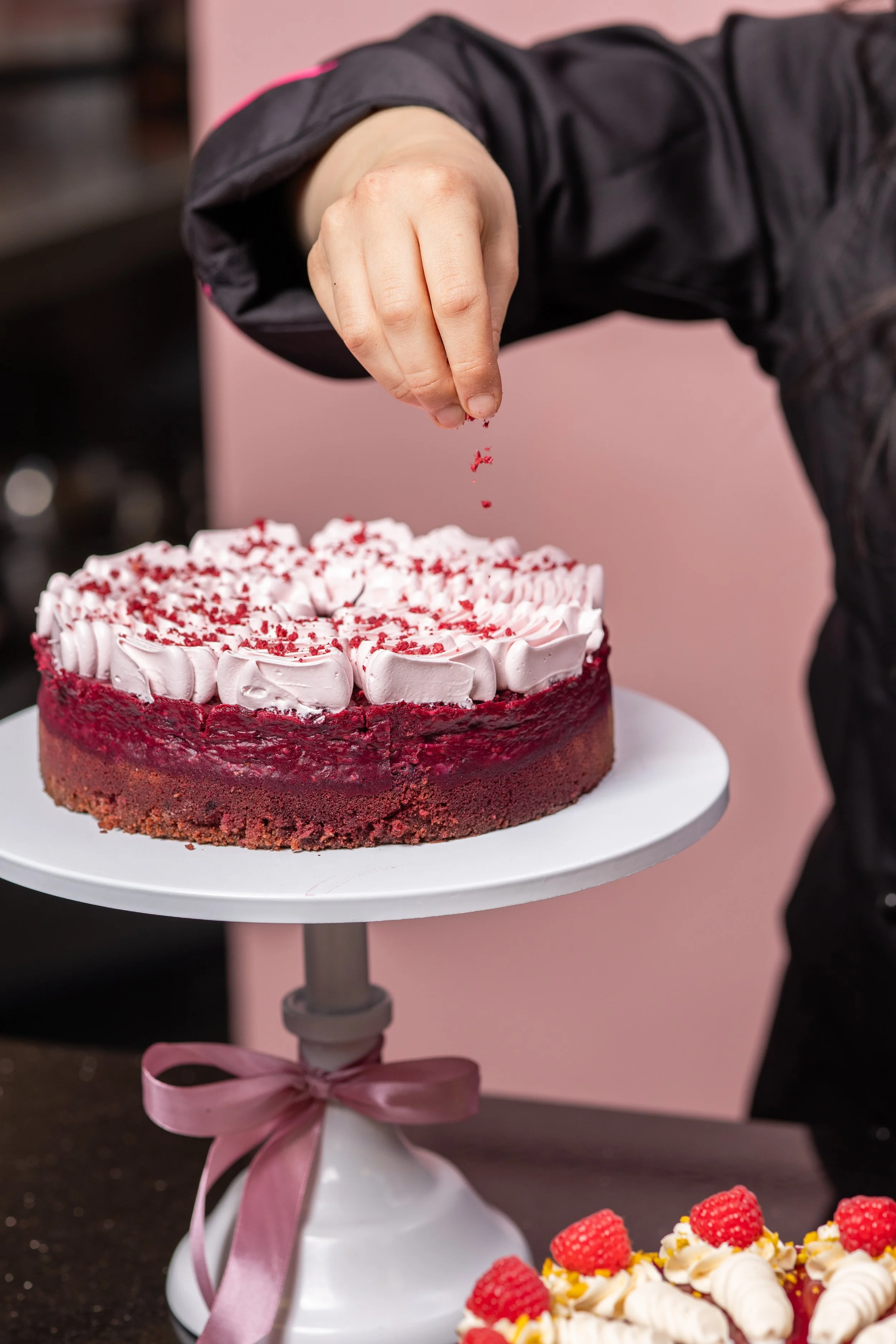 Person dekoriert eine Torte mit roten Streuseln.