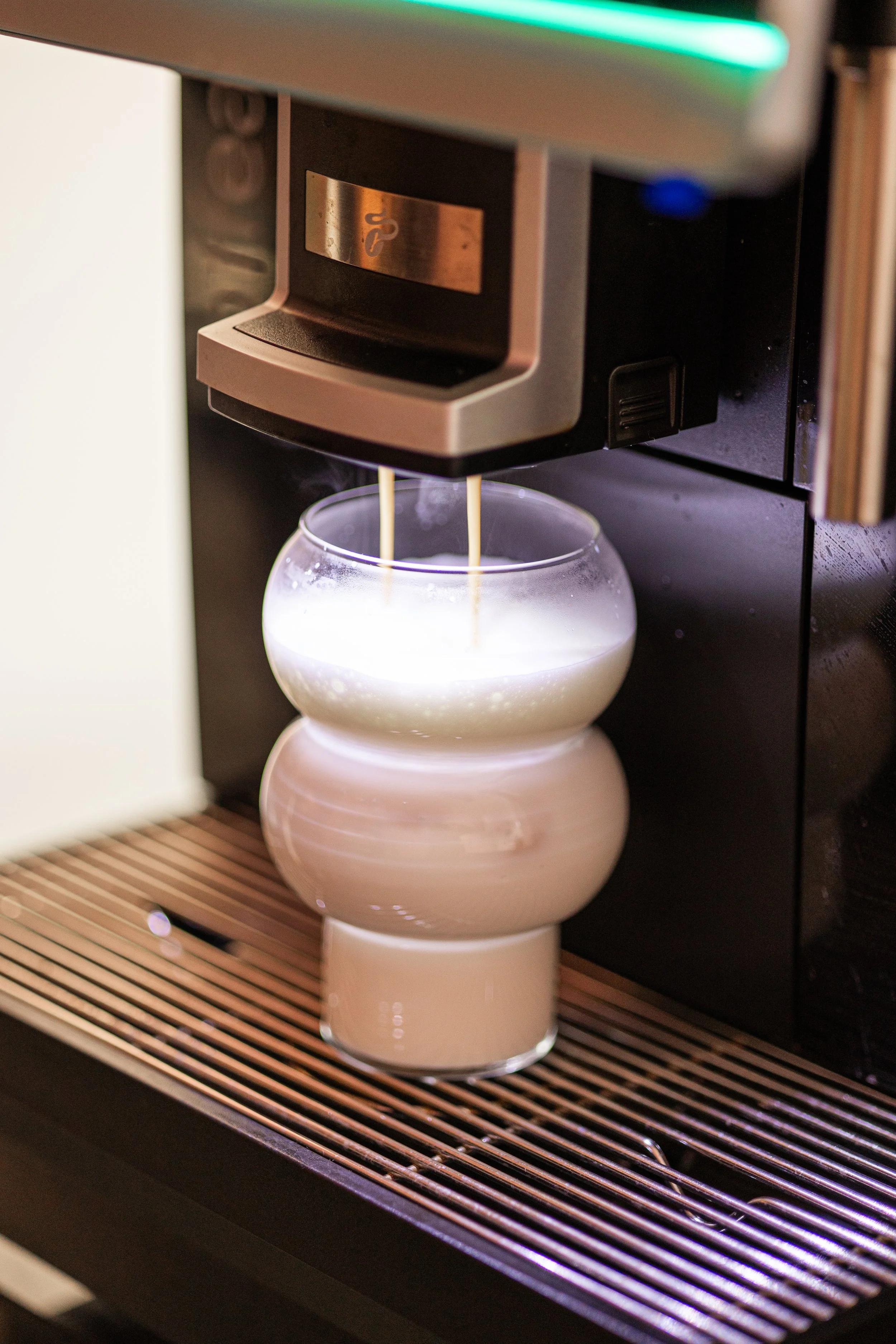 Ein Kaffeeautomat gießt Milch in ein stilvolles Glasgefäß mit einer modernen, gestuften Form.