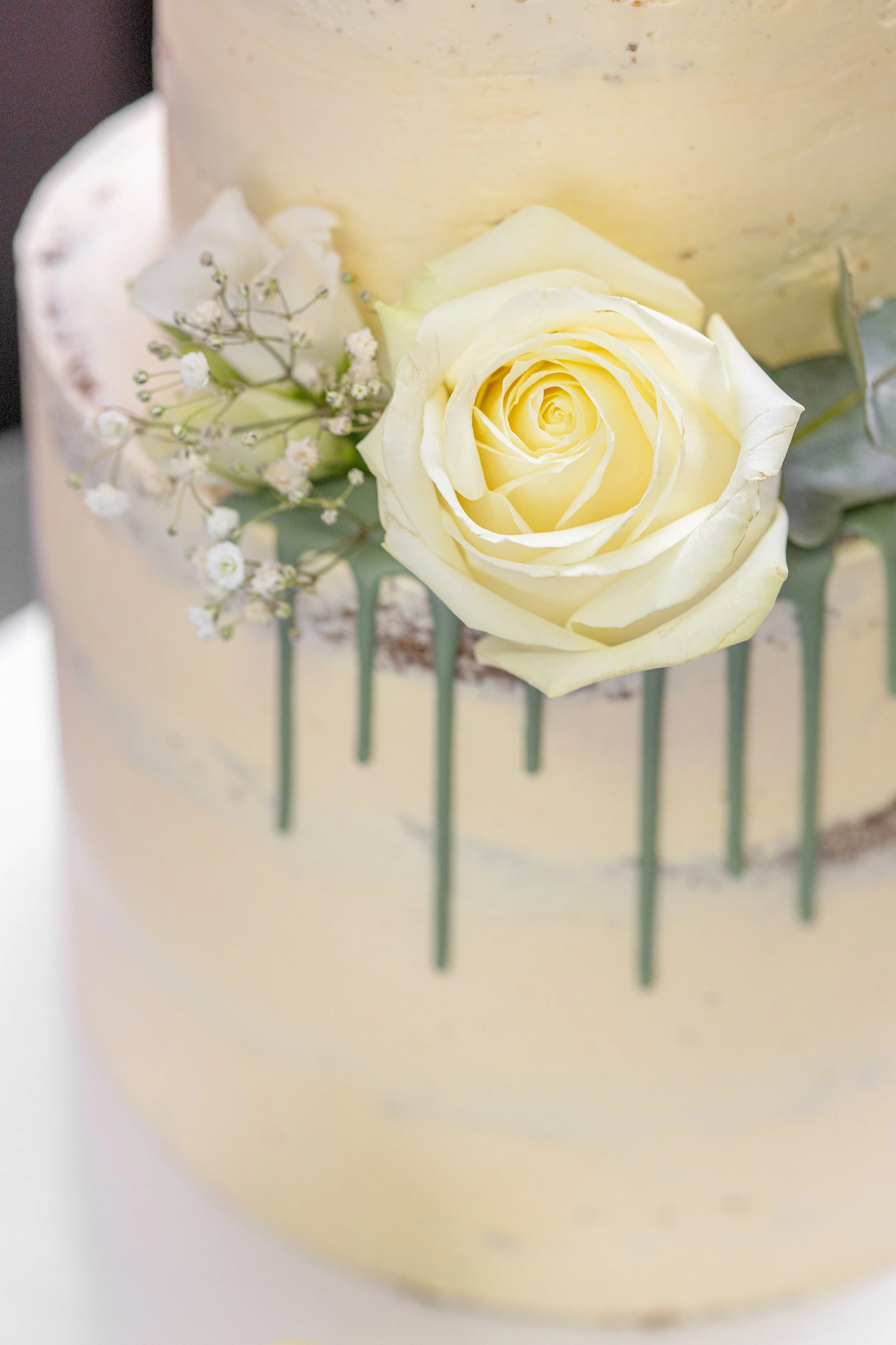 Nahaufnahme einer Hochzeitstorte mit weißer Rose und kleinen weißen Blumen als Dekoration.