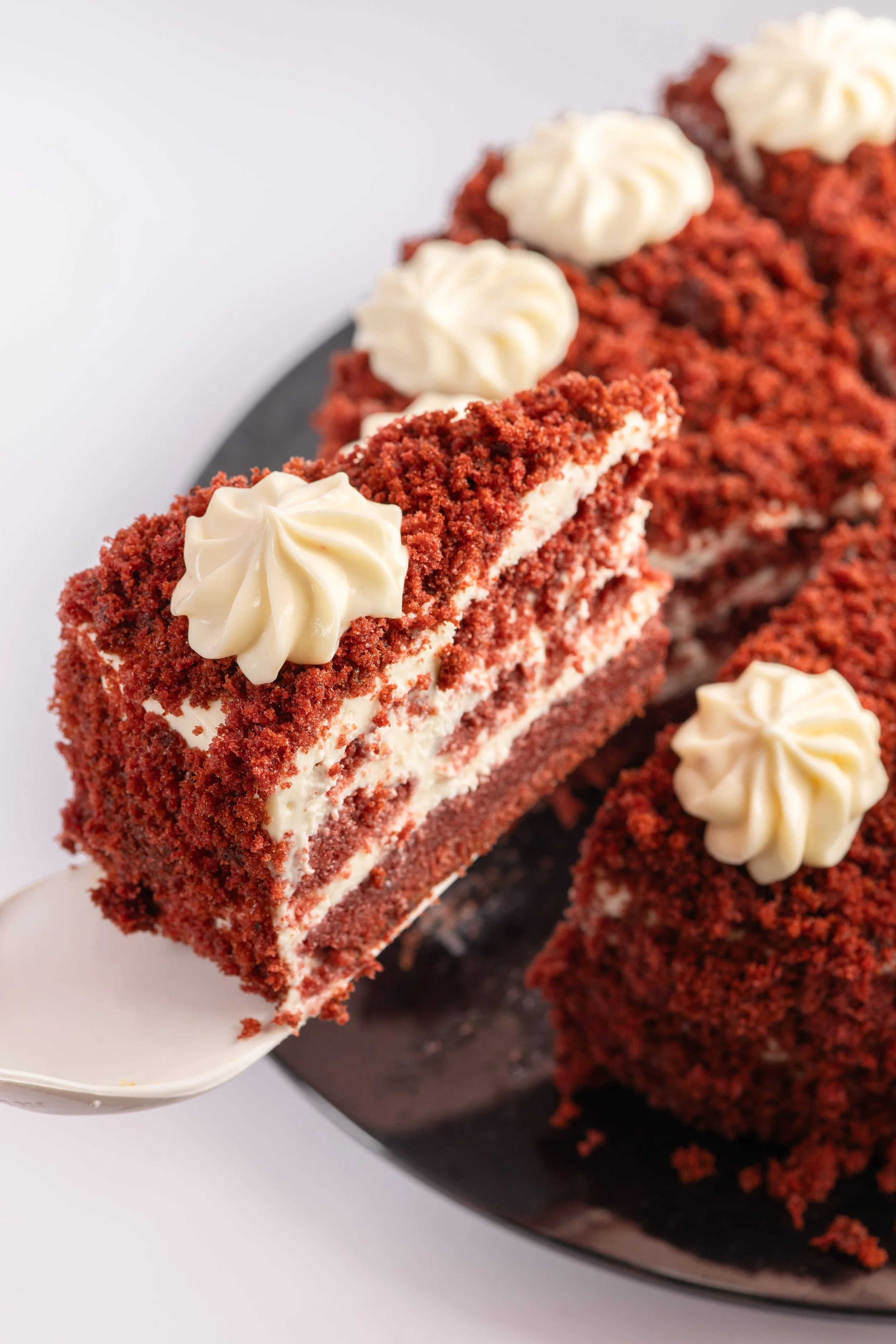 Ein Stück roter Kuchen mit Vanillecreme und Zuckerkuchendecke auf einem schwarzen Teller.