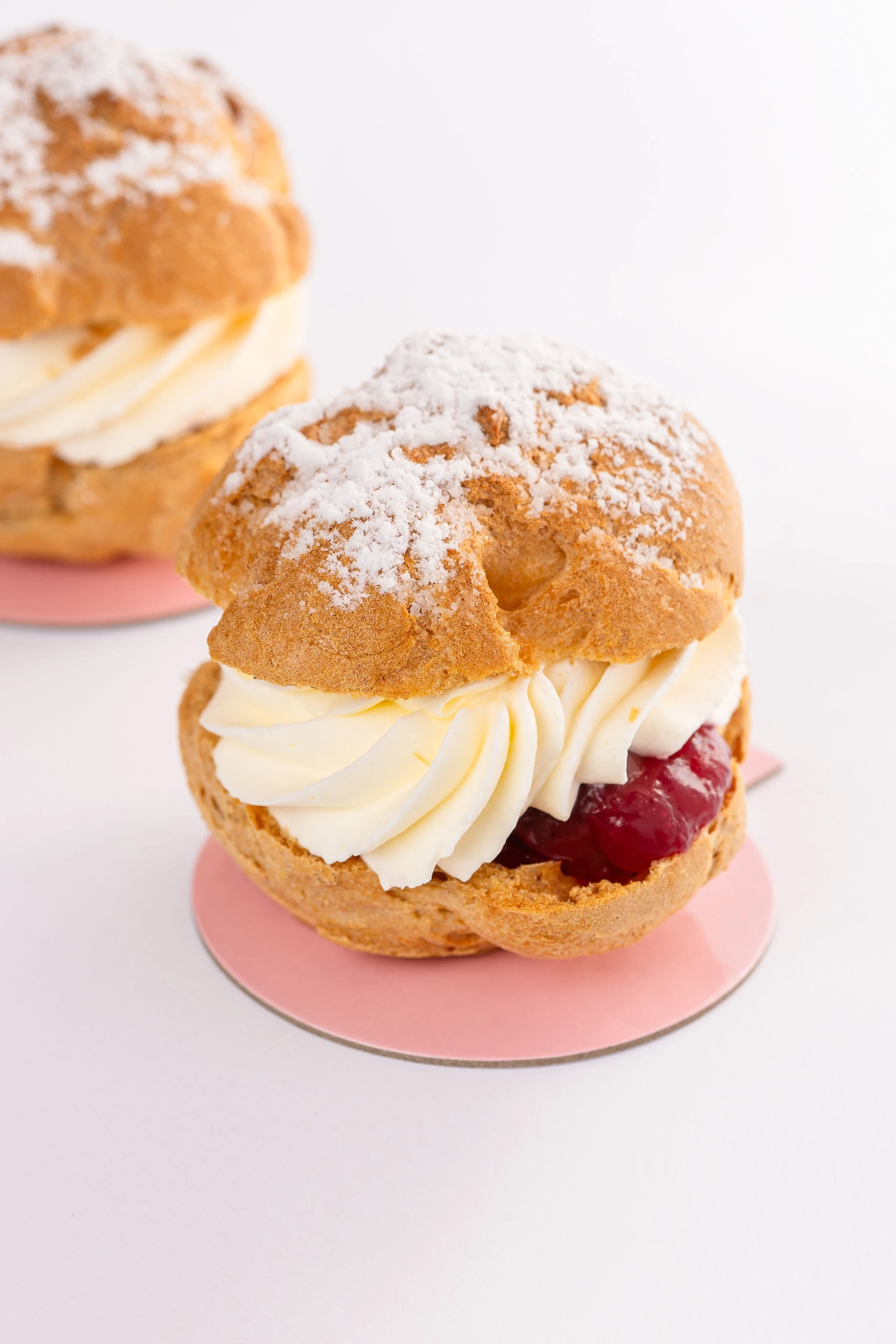 Klein zusammengesetztes Gebäck mit Schlagsahne und Marmelade, bestäubt mit Puderzucker, auf pinkem Untersetzer