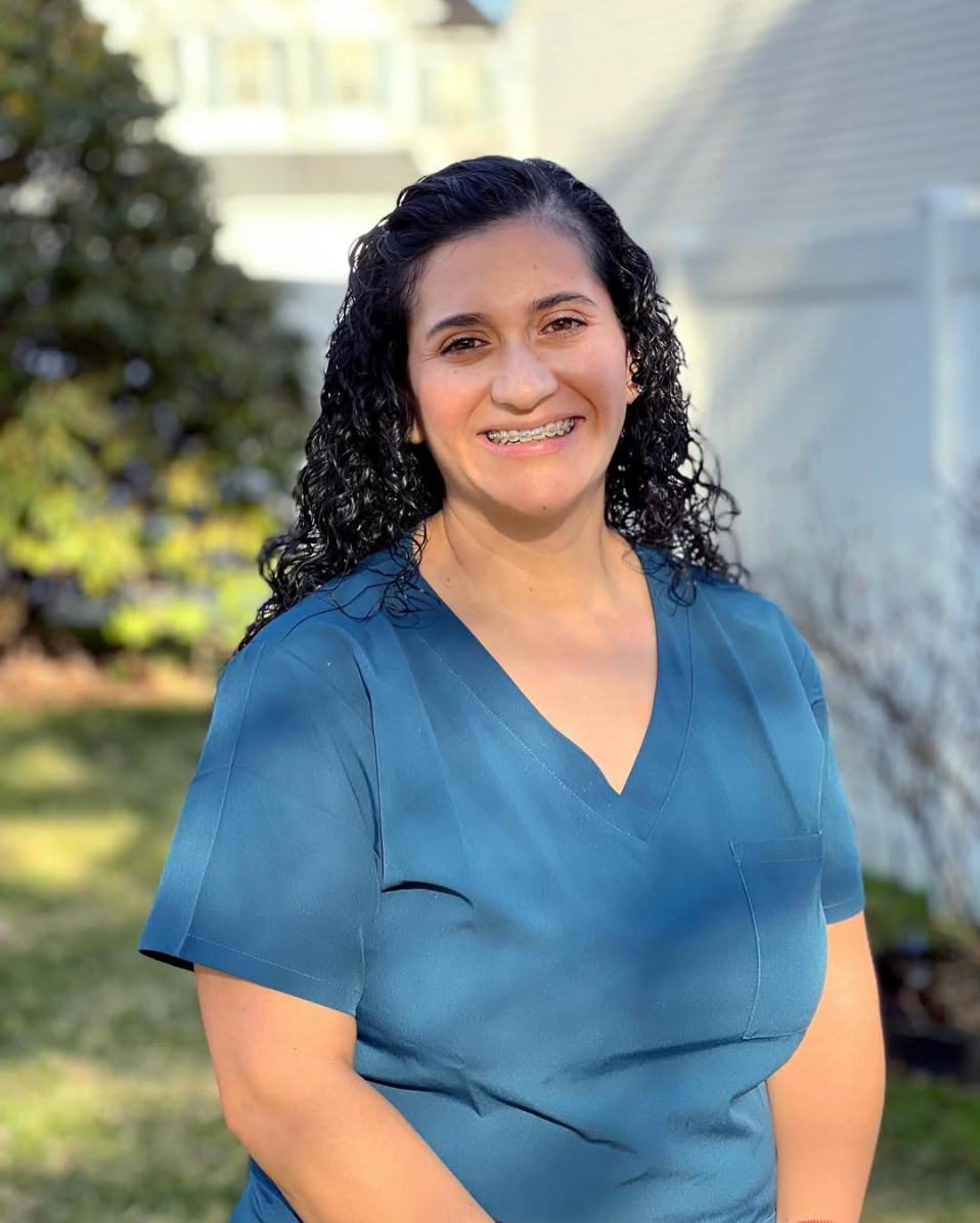 Paula Bradley sits for a headshot with dark, curly hair and a big smile and a teal scrubs shirt on. She is a maternal health and infant occupational therapist who owns Strong Roots Occupational Therapy in south NJ & Philadelphia