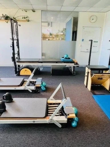 Clinical Pilates studio with specialised equipment, including reformer machines, exercise balls, and mats, in a well-lit area.