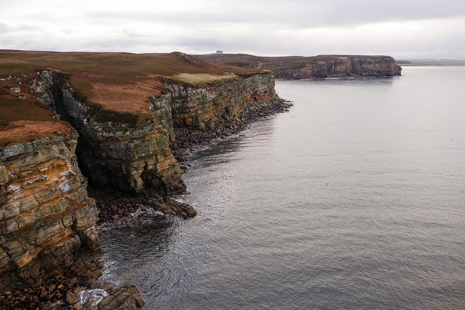 Cliffs along a shoreline with rocky bases and grassy tops, extending into the distance under cloudy skies.