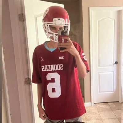 Young person taking a mirror selfie wearing a red football helmet and a maroon football jersey with the number 5.