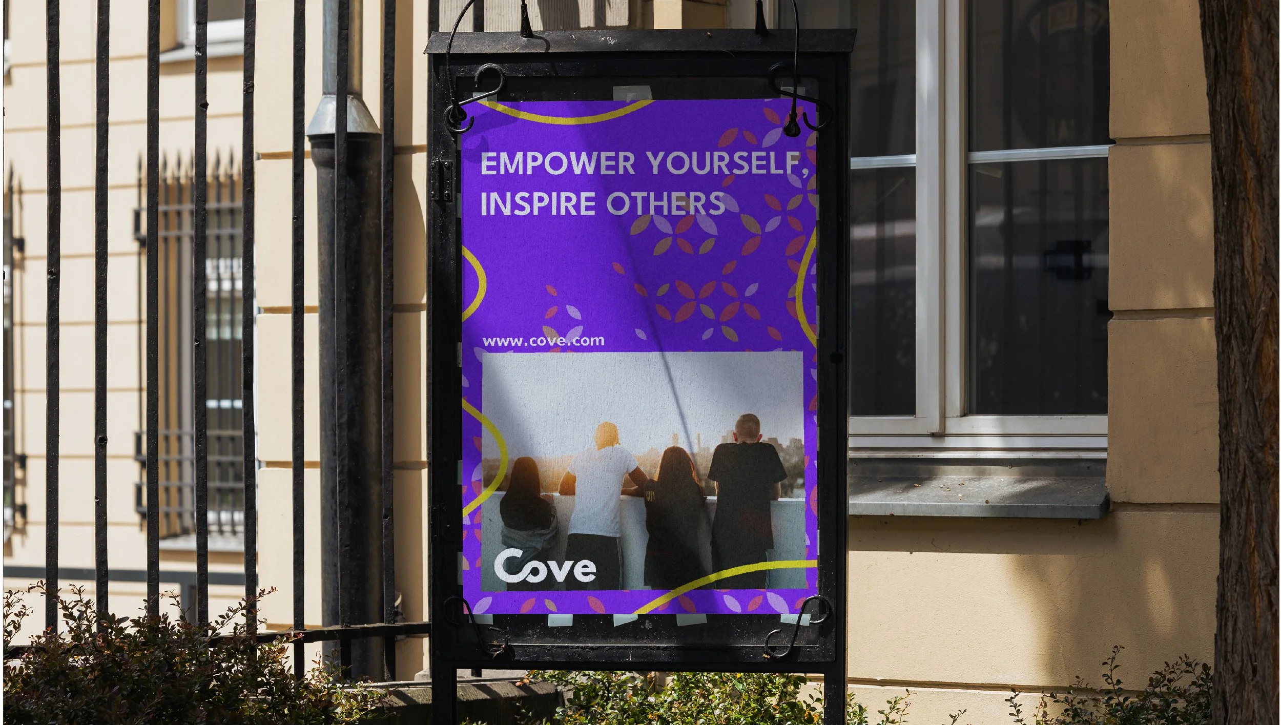 A billboard on a black stand shows a purple background with the message "Empower Yourself, Inspire Others" and a website address. The lower part displays four people at a balcony at sunset, looking at the view with their backs to the camera.
