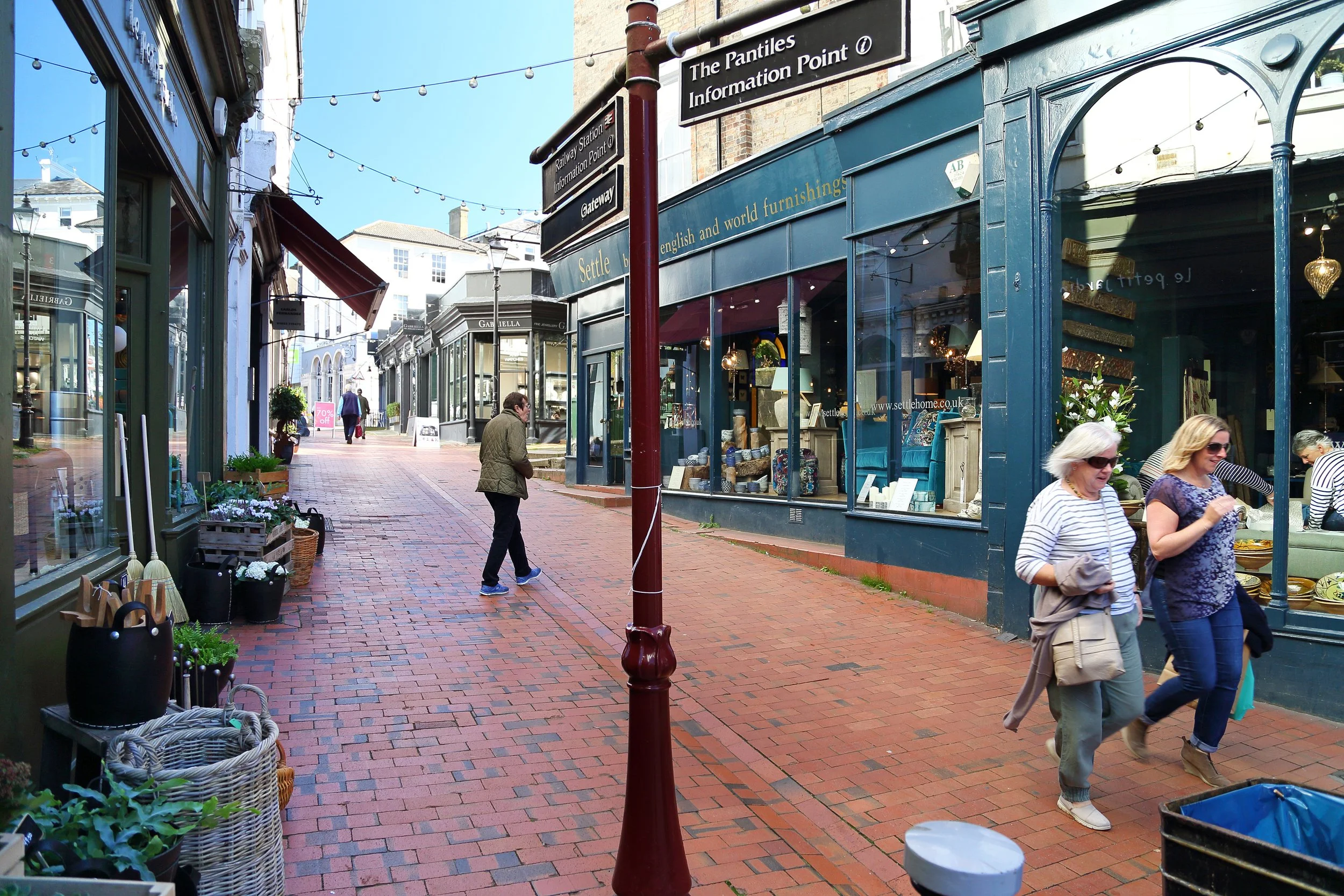 People shopping along a brick-paved street lined with shops and window displays in a European town.
