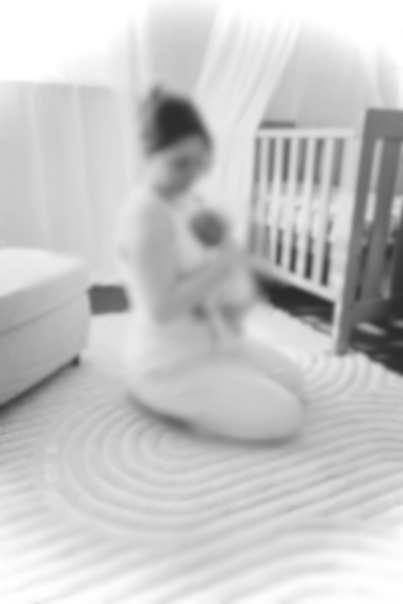 A woman kneeling on the floor, holding a baby, in a nursery with a crib and curtains.