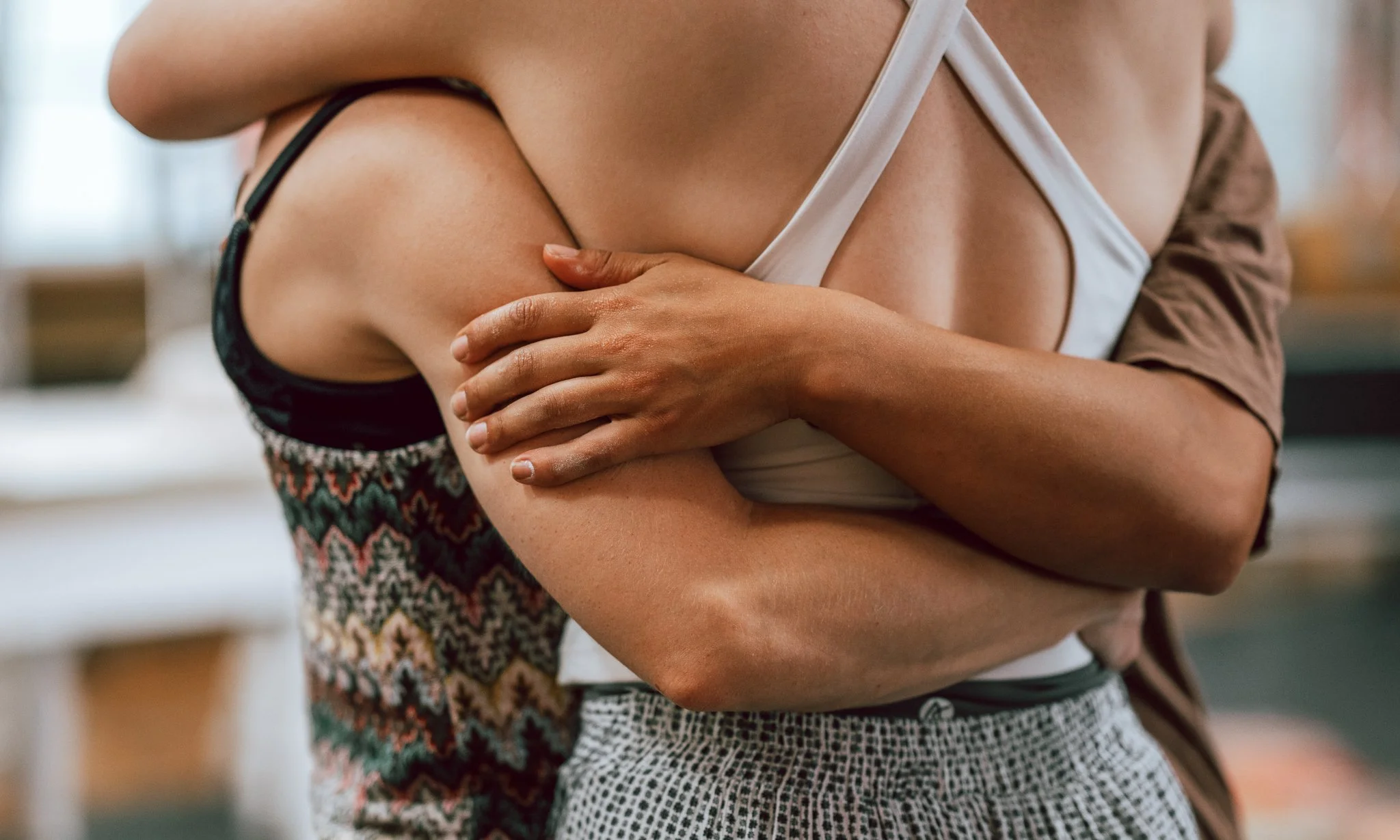 Close-up of two people hugging, with one person's arm wrapped around the other's shoulders in an indoor setting.