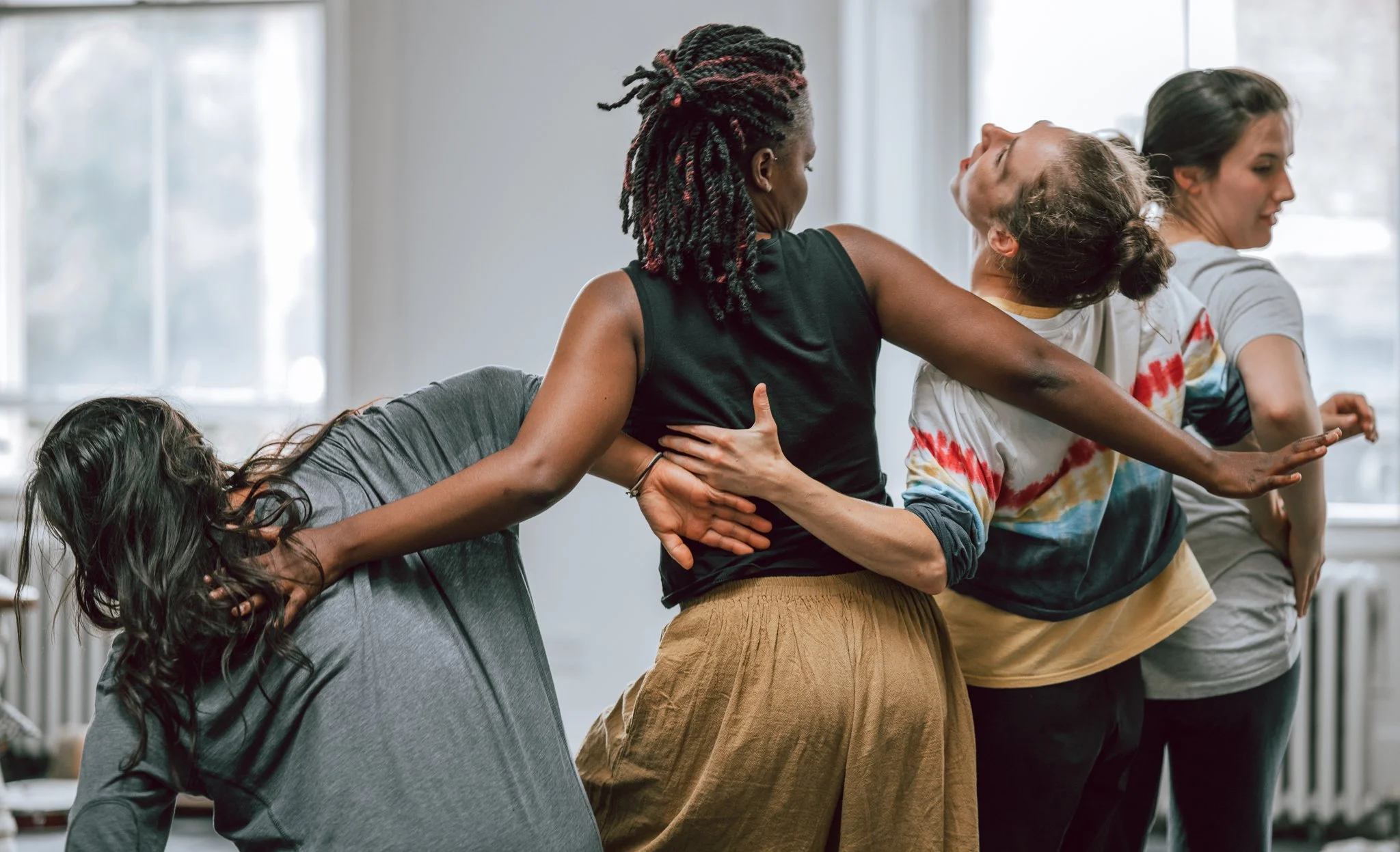 Group of women performing a team-building activity, supporting each other by holding and leaning on their friends' backs and shoulders.