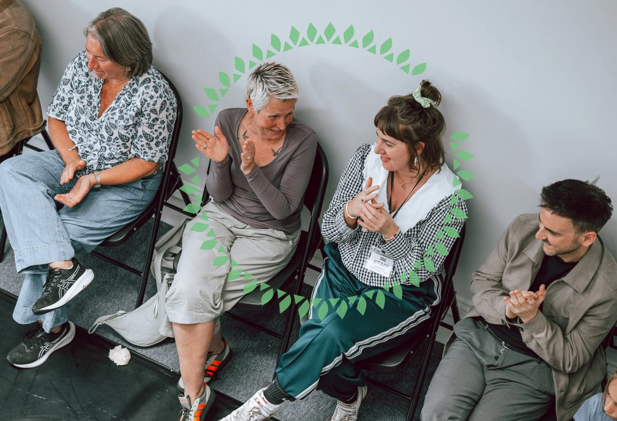 A group of diverse people sitting in chairs in a waiting area, engaged in conversation and smiling.