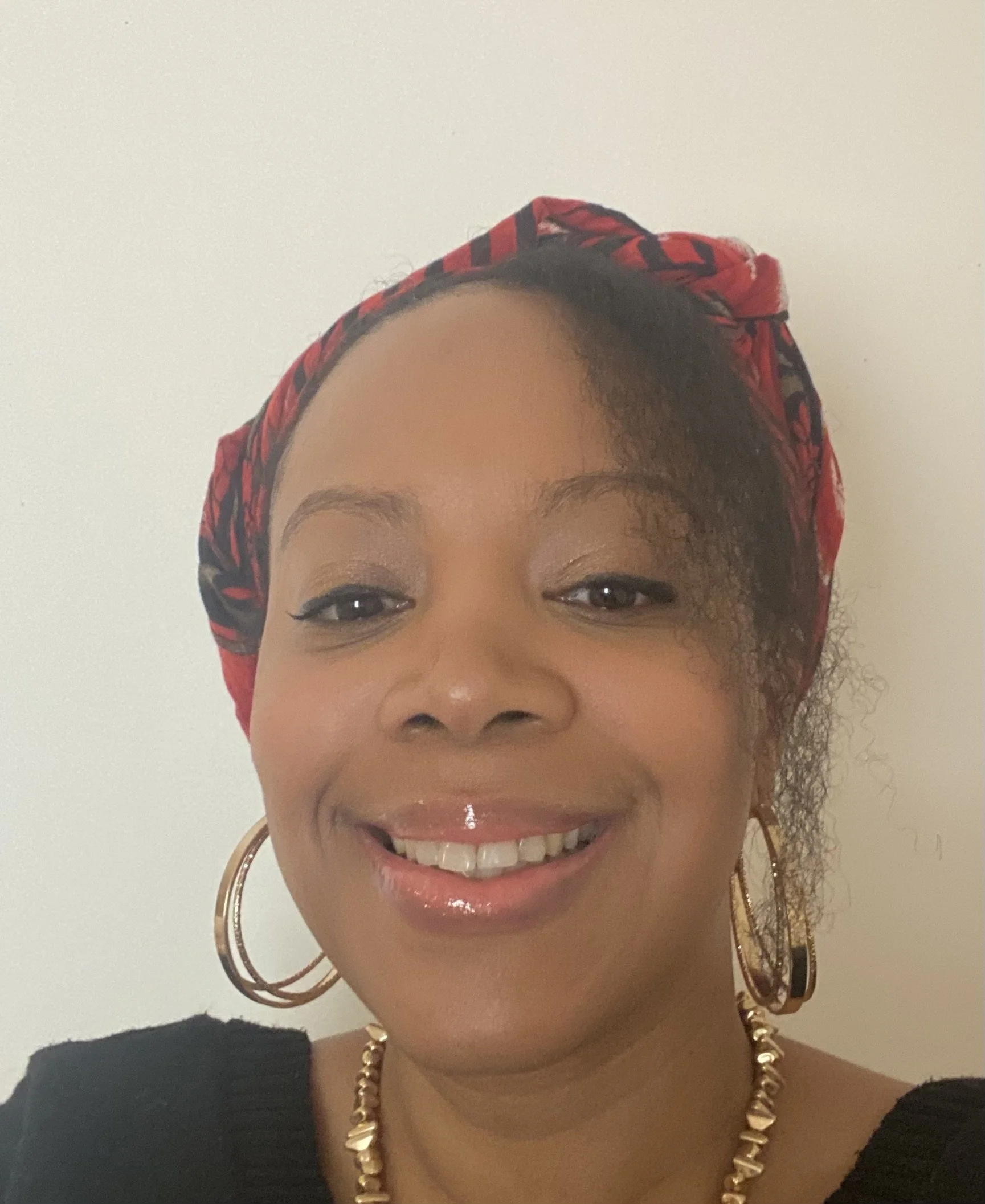 L'autrice Macha Meril souriante portant un foulard rouge et noir, des hoop en or, et une chaîne en or, avec une étape partielle de son visage visible.
