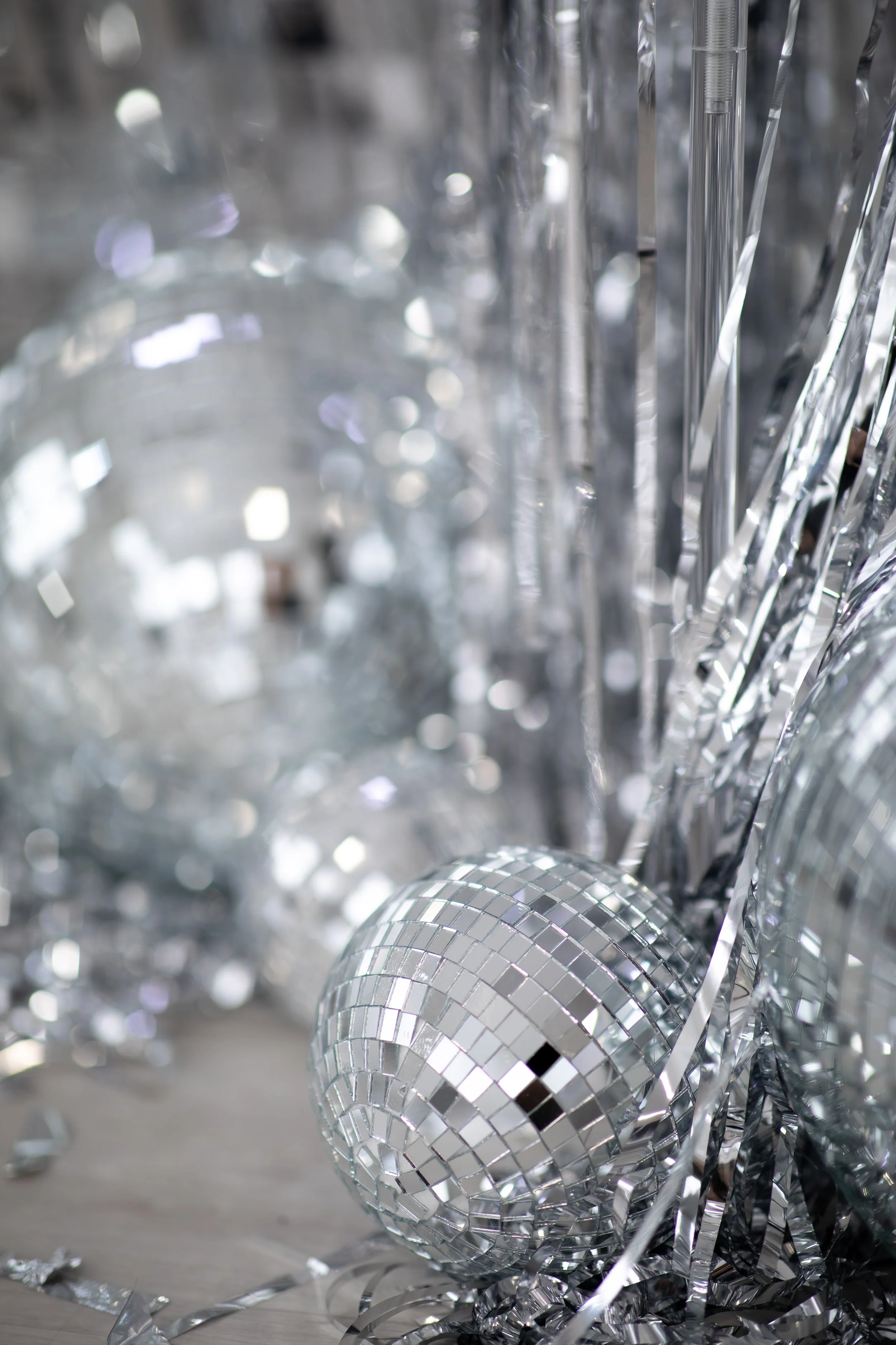 Close-up of shiny silver disco ball ornaments and metallic streamers on the floor.