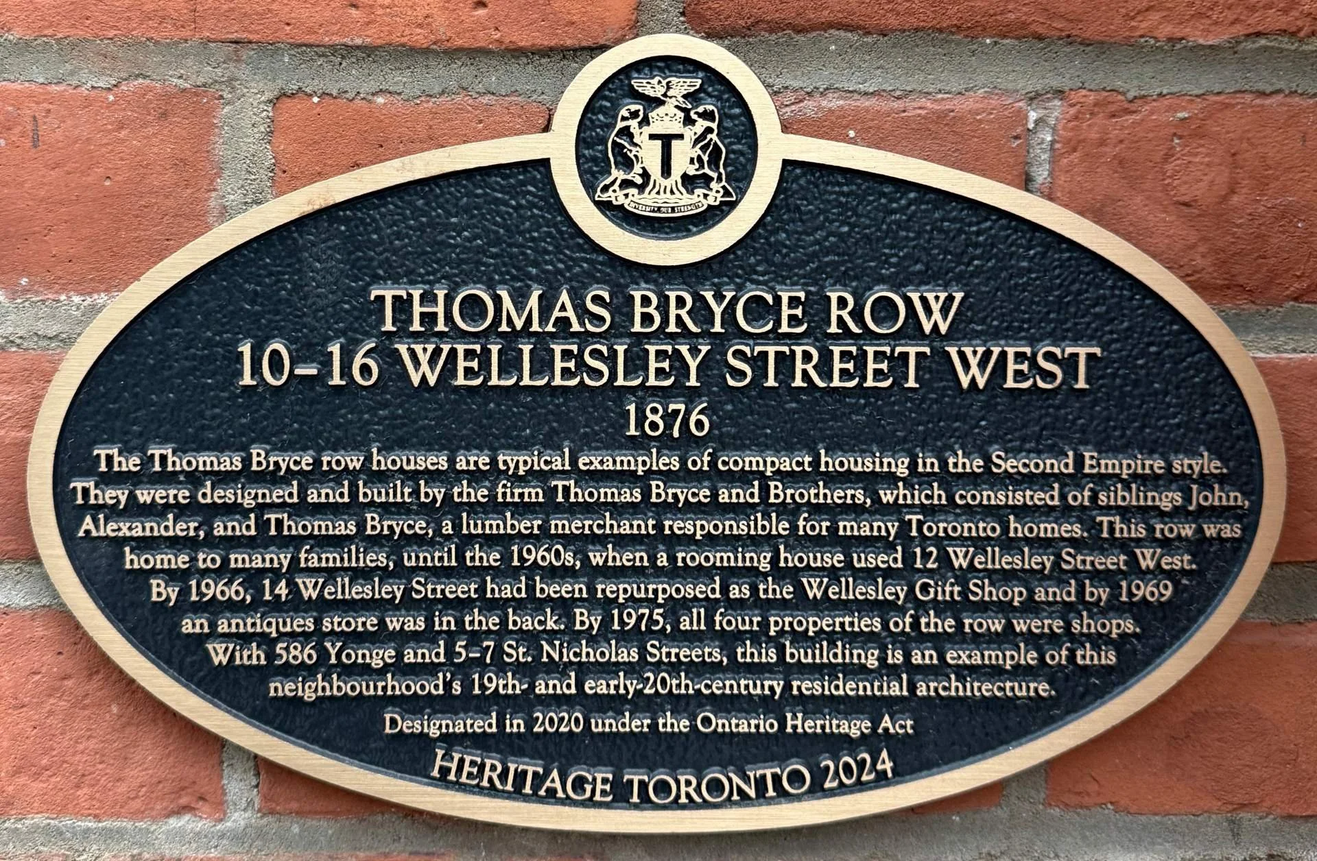 Heritage Toronto 2024 plaque on the exterior brick of Thomas Bryce Row, 10–16 Wellesley Street West, Toronto. The plaque reads: Thomas Bryce Row, 10–16 Wellesley Street West, 1876. Designated in 2020 under the Ontario Heritage Act.