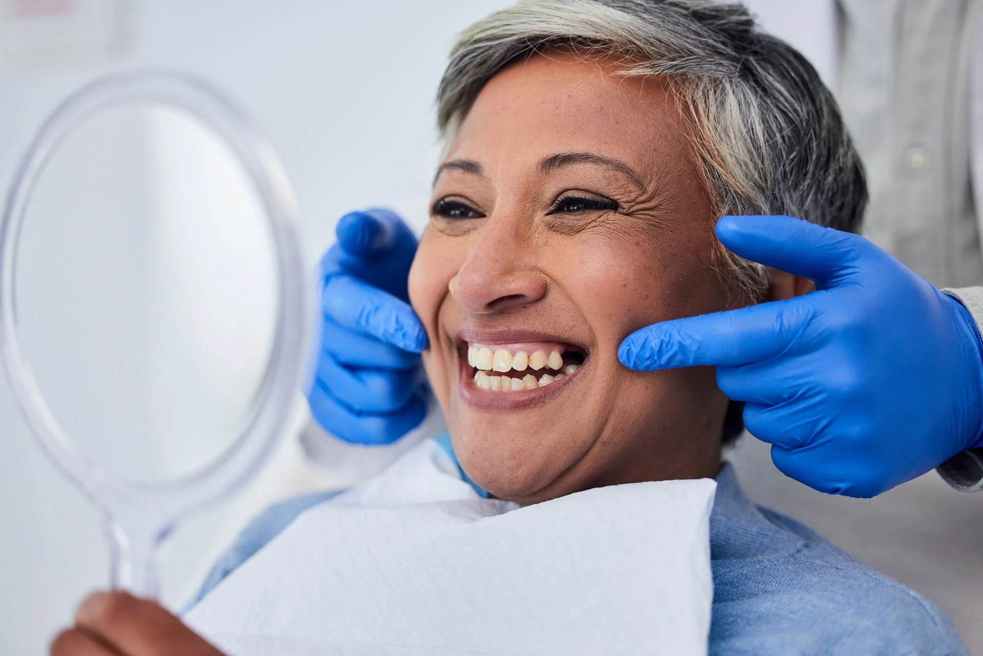 Patient reviewing her smile in a mirror during a dental consultation.