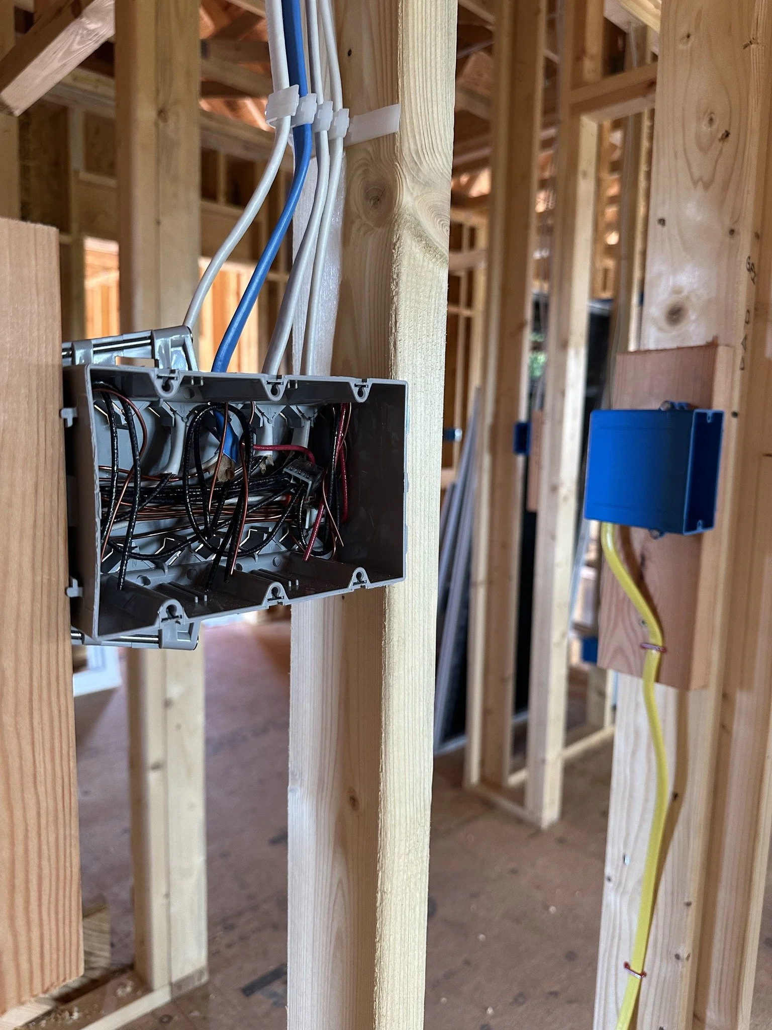 Electrical wiring inside a construction site wall with an open gray electrical box and blue, white, and yellow wires.